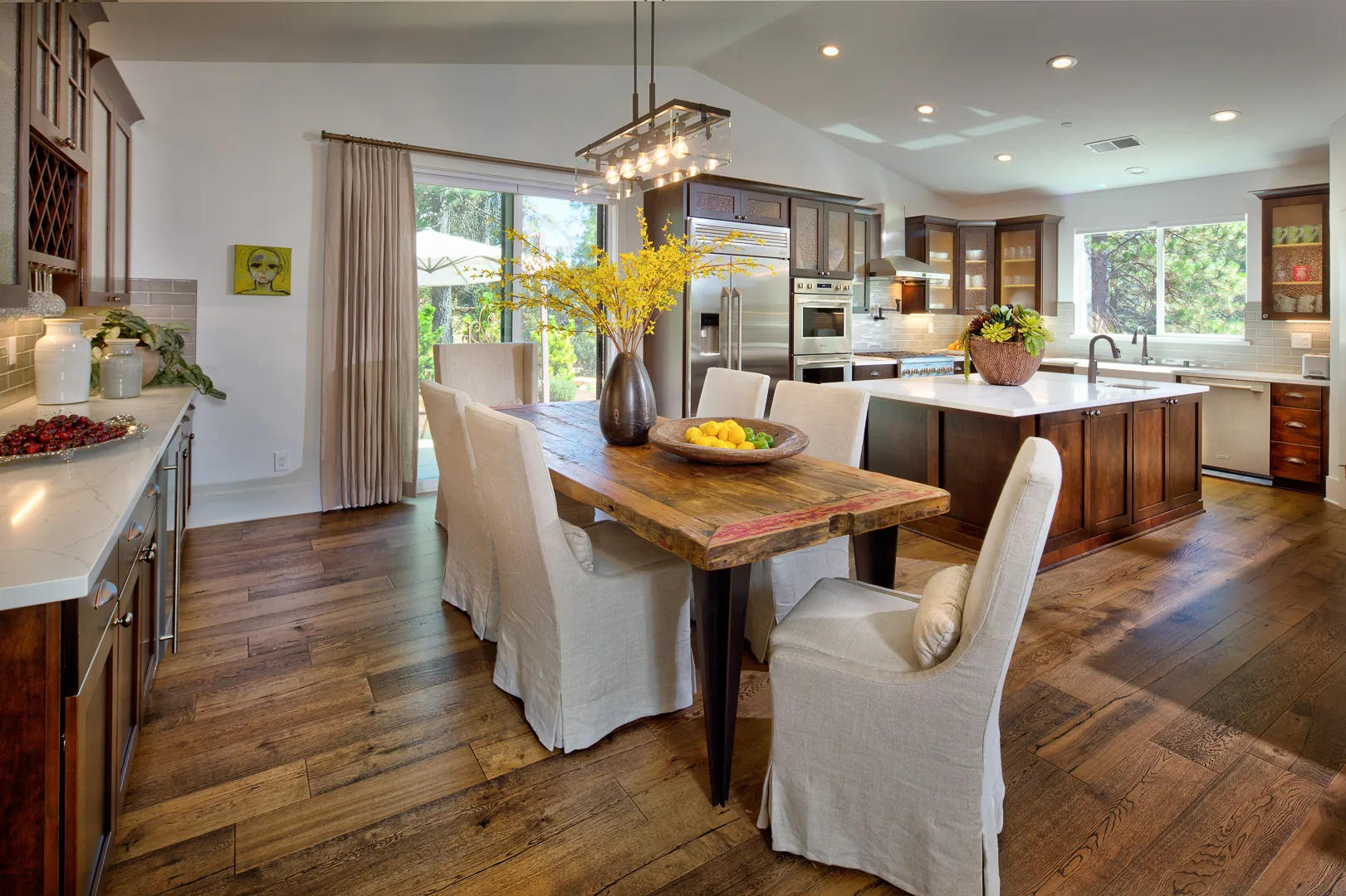 Open kitchen and dining area with reclaimed wood table, linen chairs, and wide-plank oak floors
