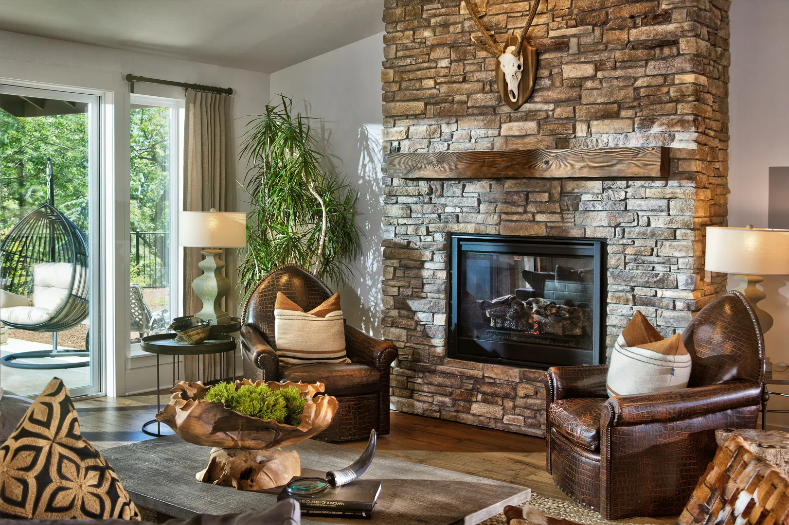Stone fireplace flanked by leather armchairs, with a hanging egg chair on the patio beyond