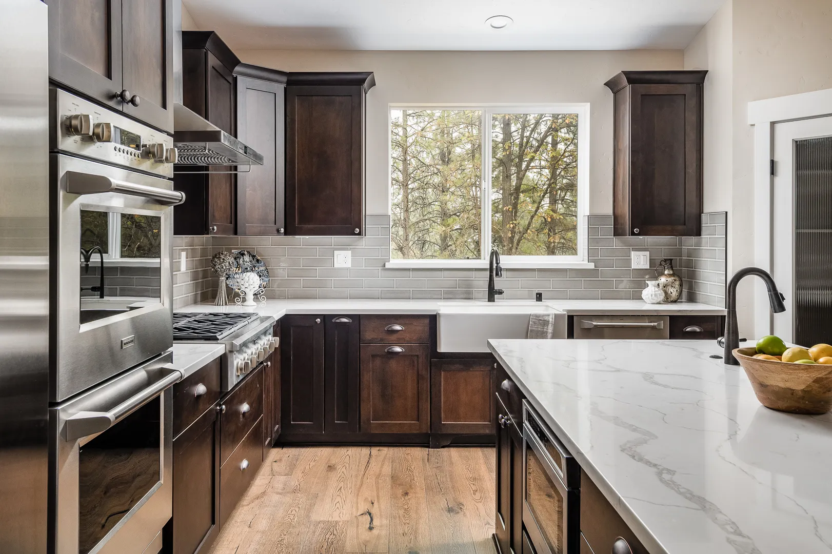 Kitchen with farmhouse sink, gray subway tile, and a window framing the surrounding pines