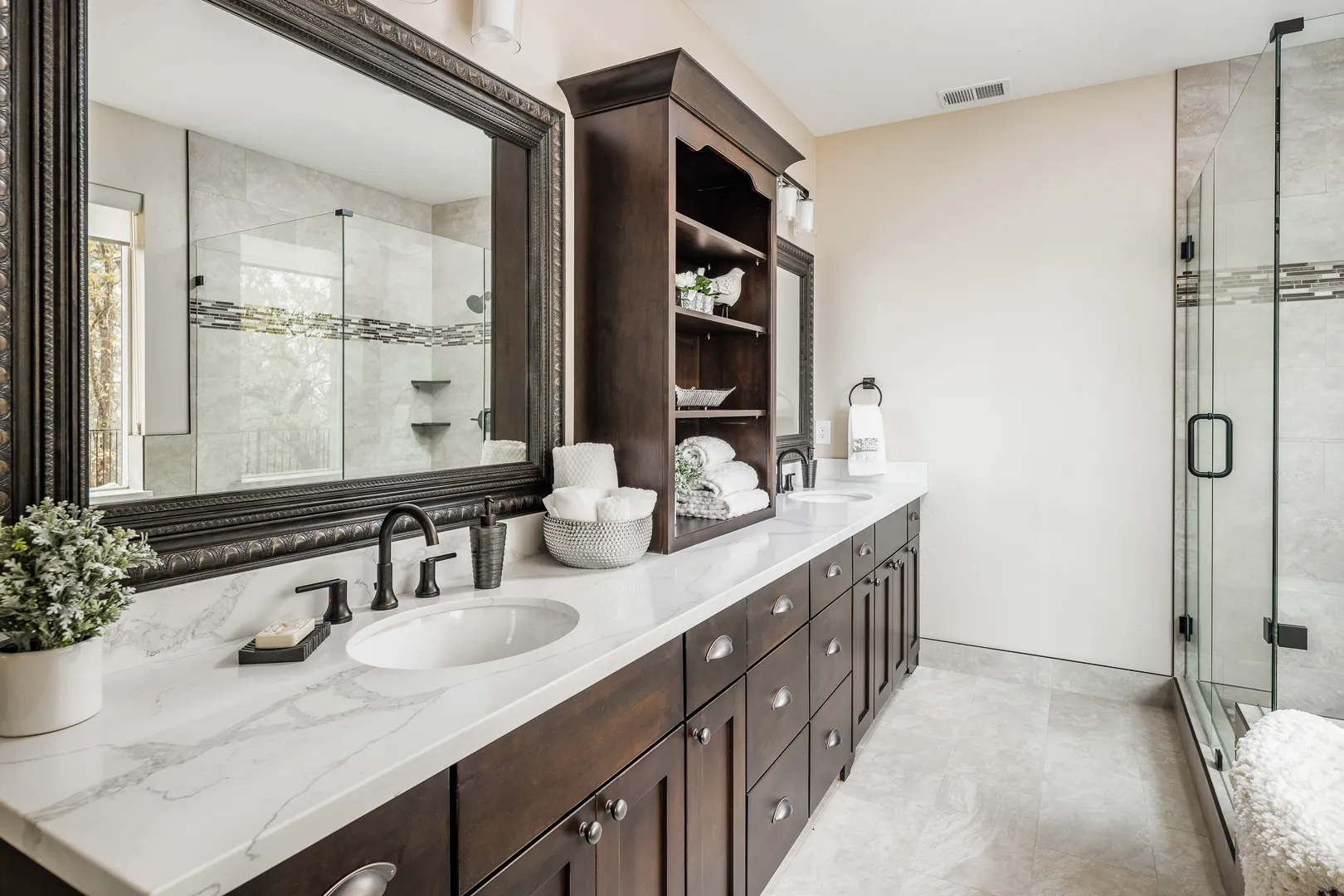 Primary bath with marble-look double vanity, framed mirrors, towel hutch, and glass shower