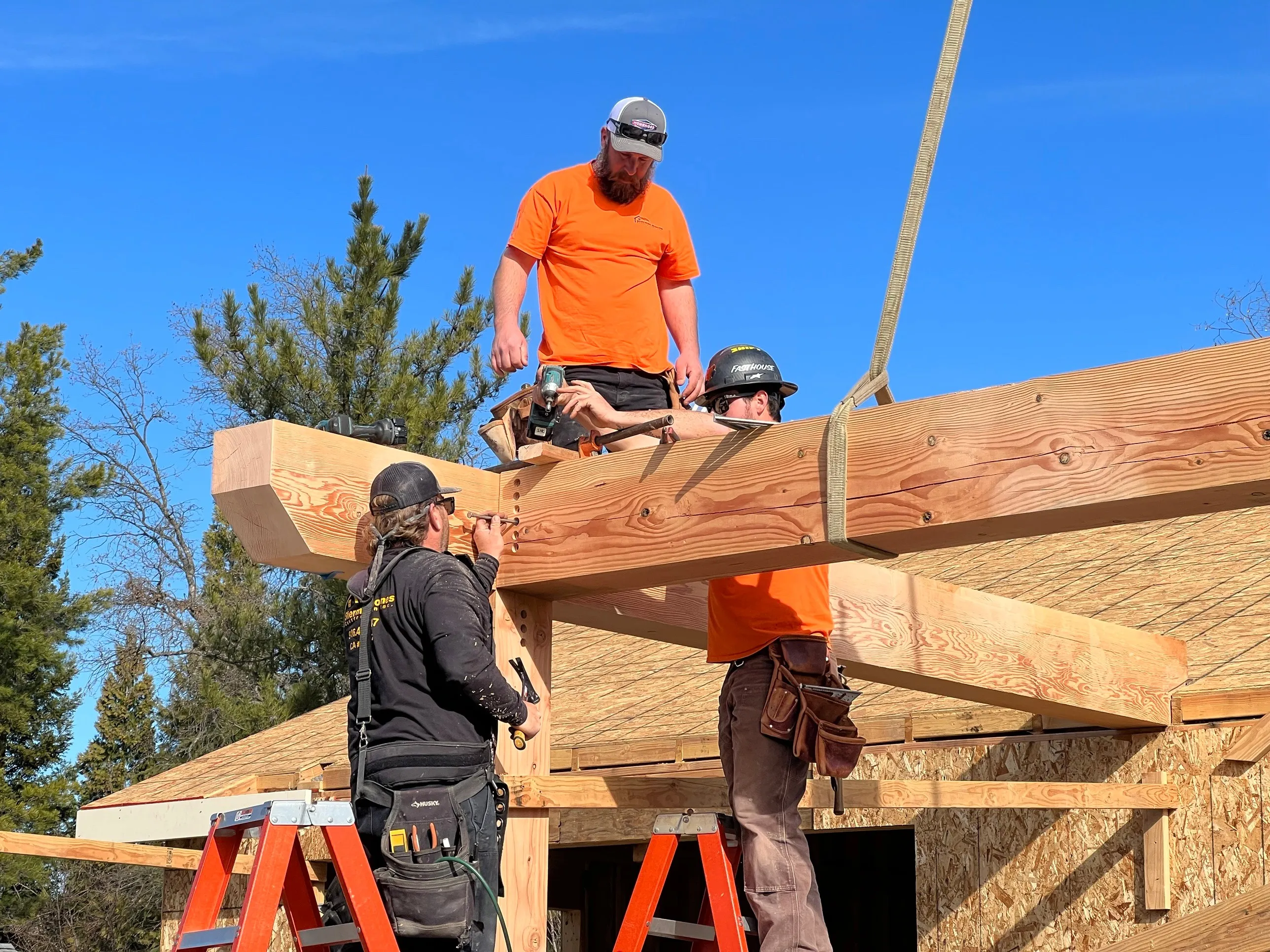 Sherman crew setting a Douglas fir timber beam on a foothill build under a clear blue sky