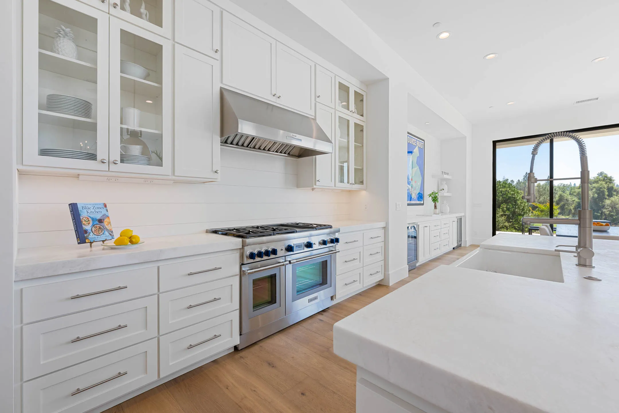 Kitchen wall with professional gas range, stainless hood, and glass-front uppers