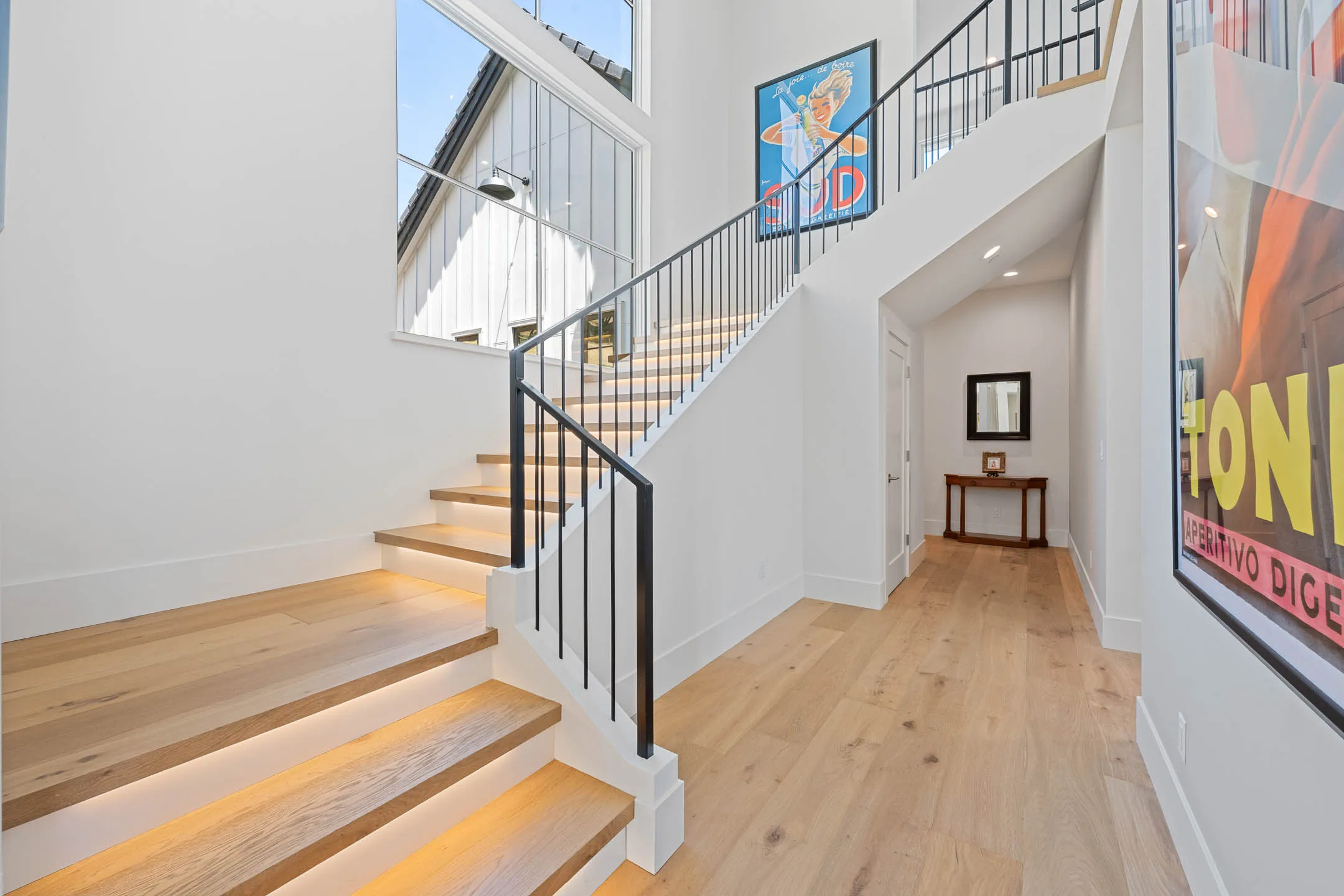 Oak staircase with underlit treads, iron balusters, and a two-story window to the courtyard in a Sherman custom home