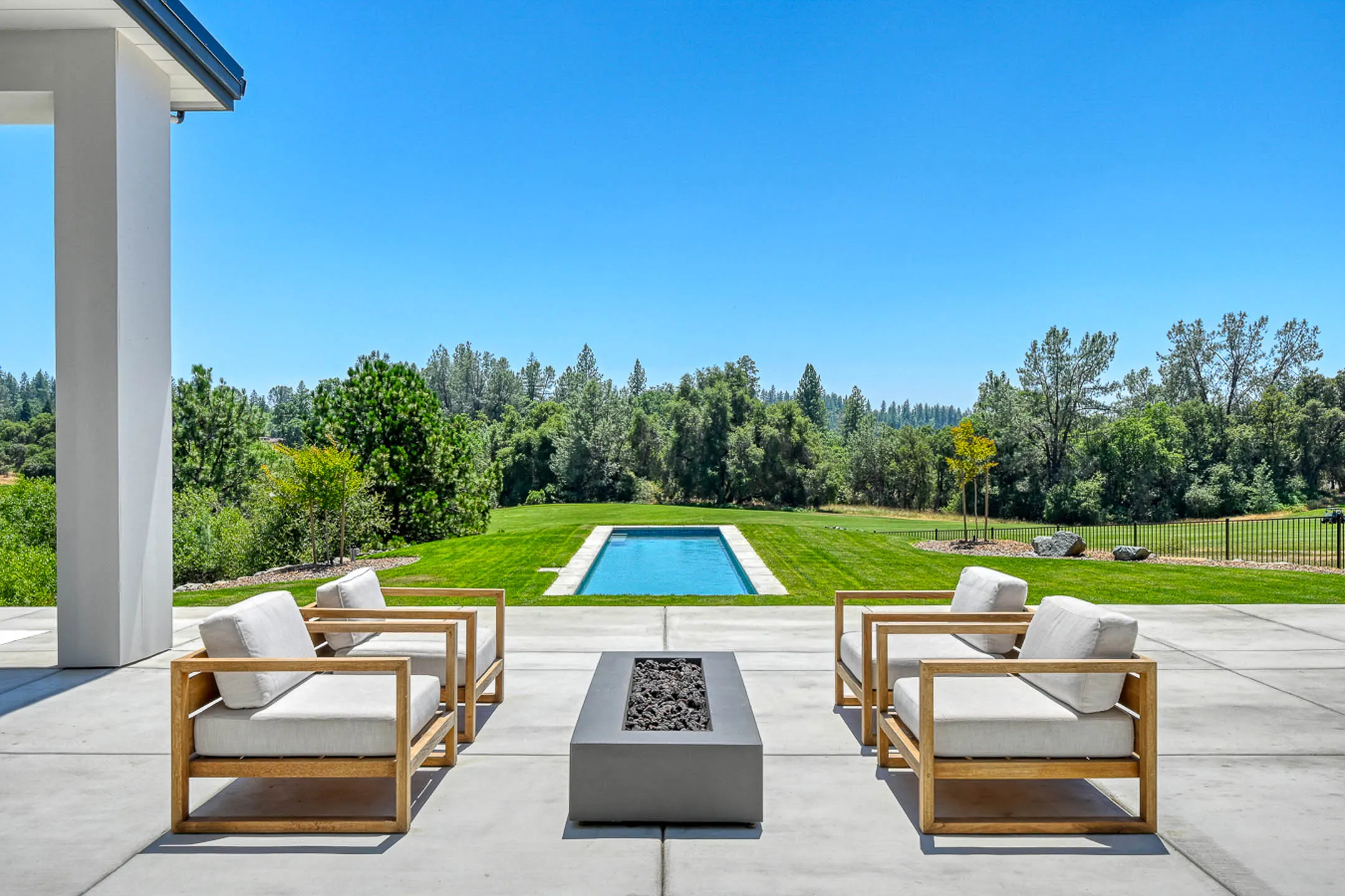 Covered patio lounge with teak chairs and a gas fire pit facing the lap pool at a Sherman custom home