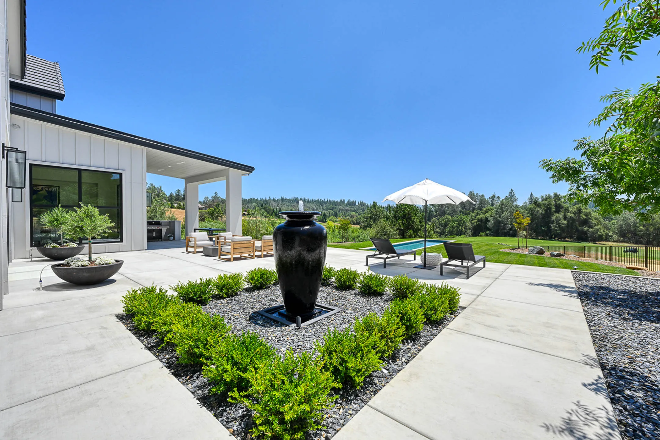 Backyard patio with urn fountain, boxwood parterre, and loungers by the pool at a Sherman custom home