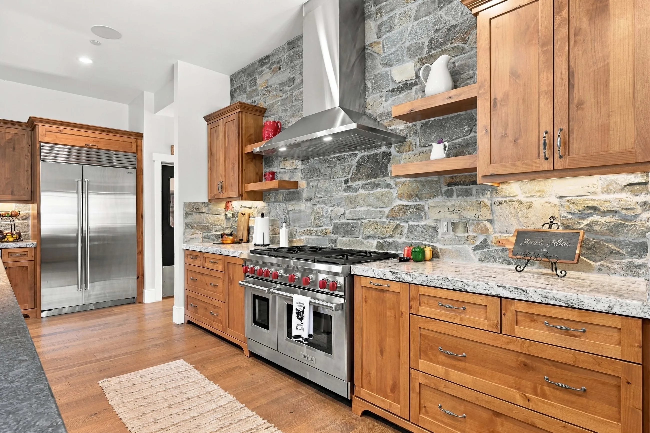 Professional range and stainless hood against stacked stone beside a built-in refrigerator