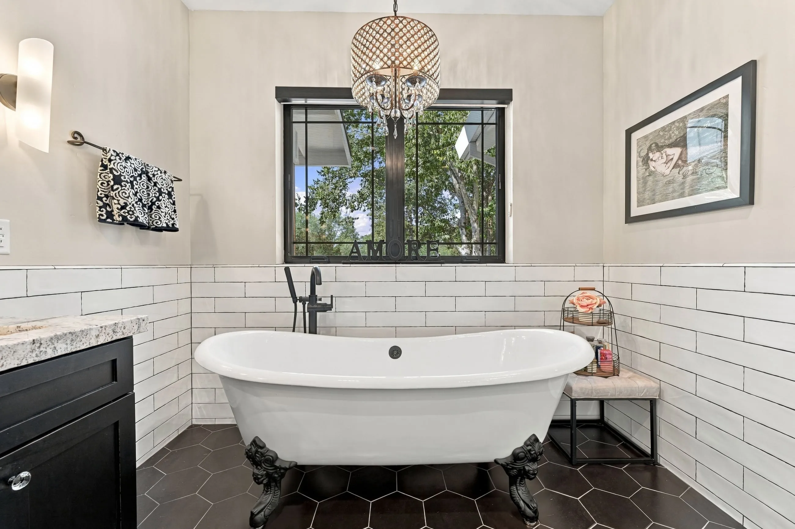 Clawfoot soaking tub beneath a black-framed window on hex tile