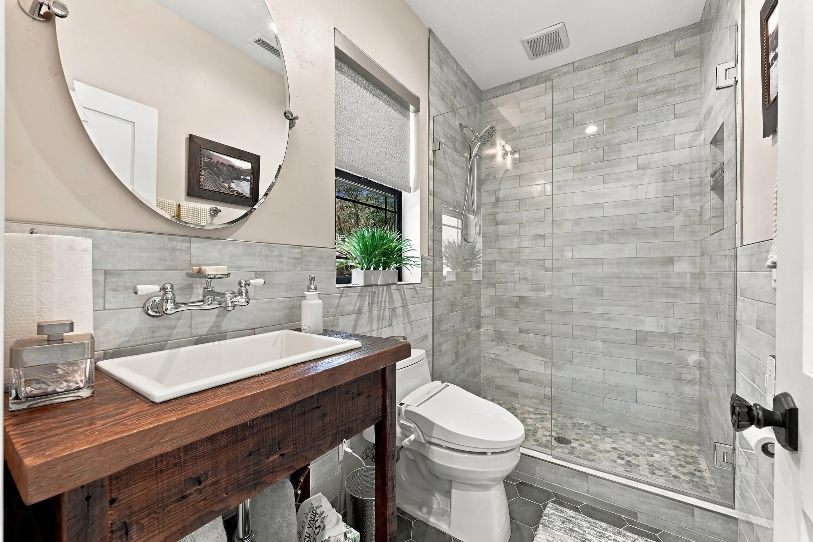 Guest bath with reclaimed-wood vanity, trough sink, and round mirror