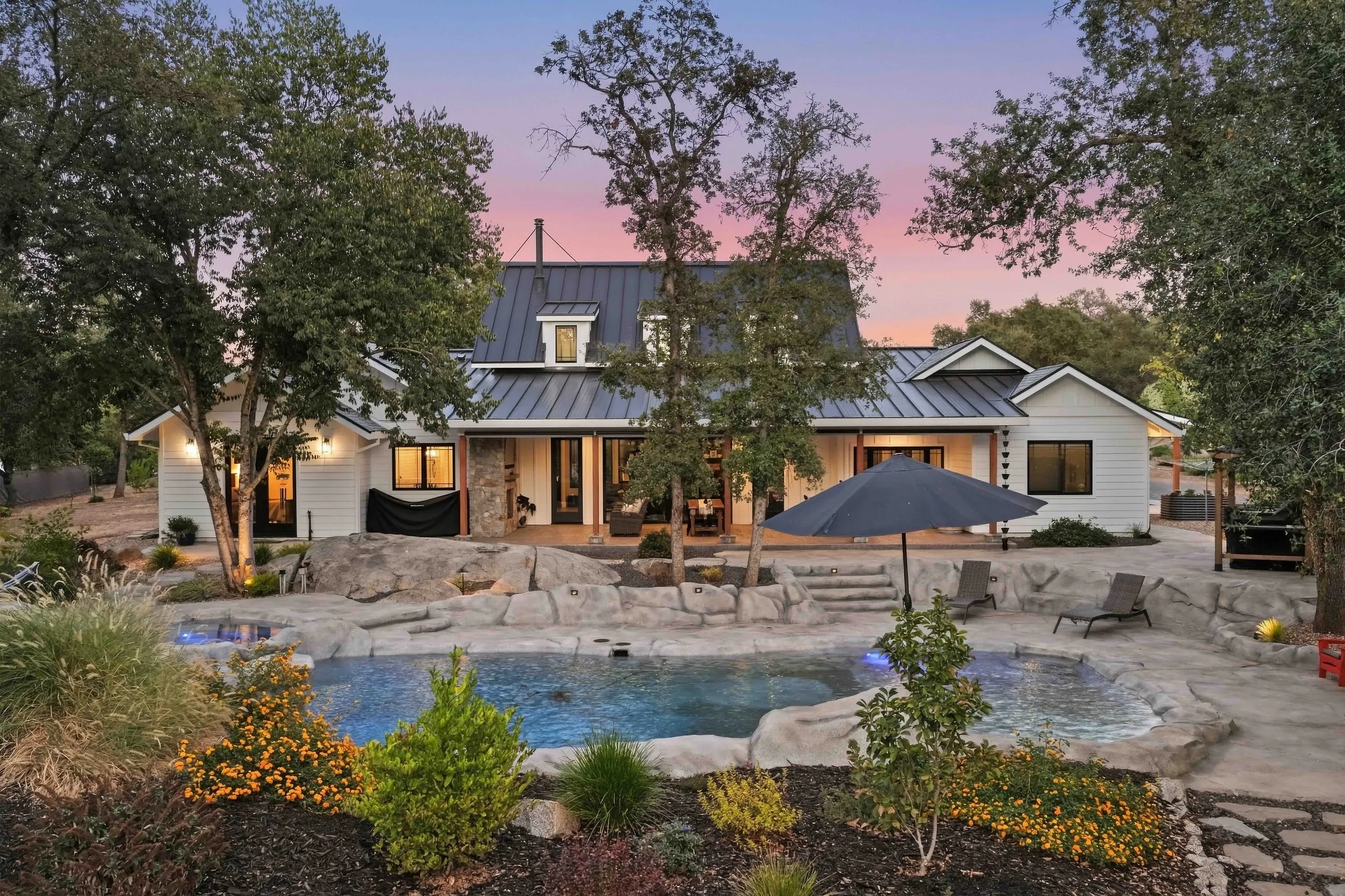 Rear elevation at twilight framed by oaks with the pool and garden in the foreground