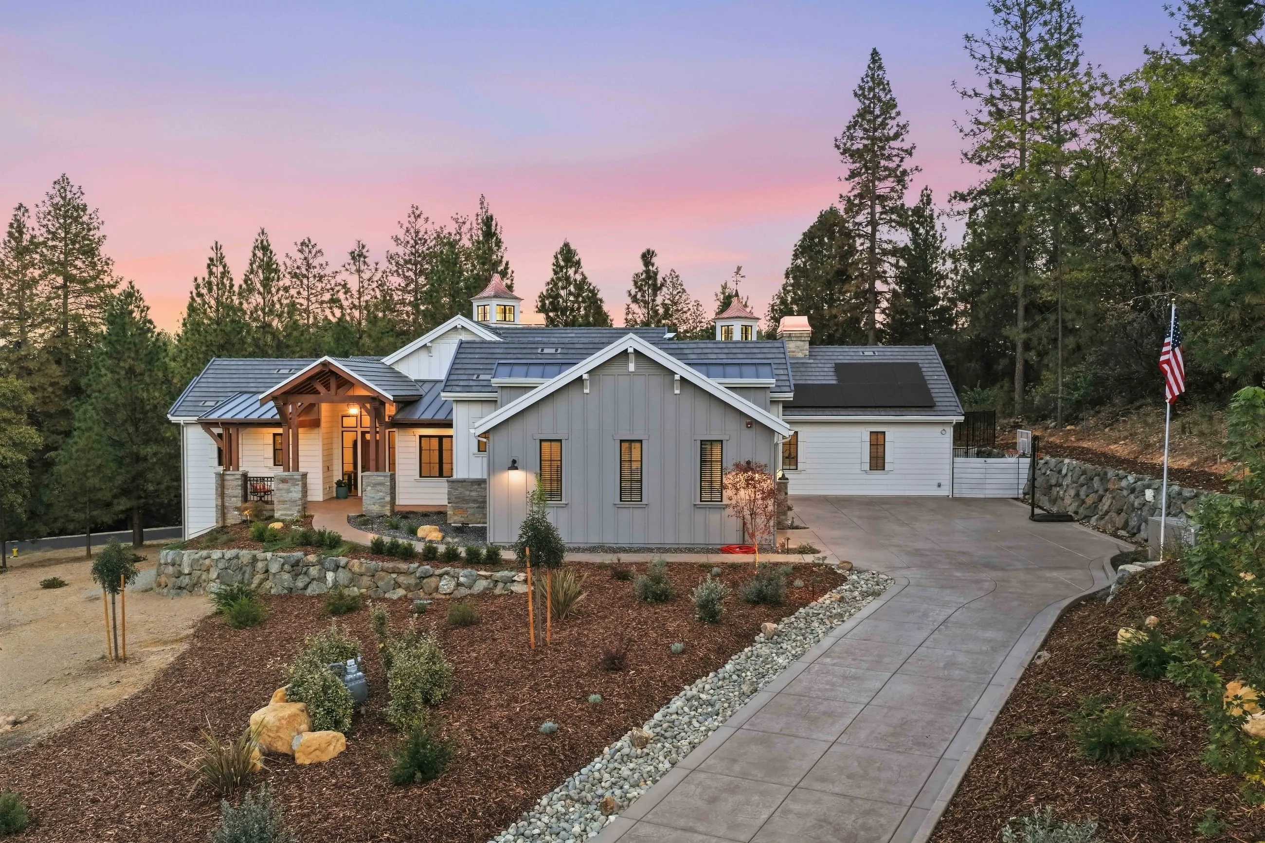 Curved driveway leading to the white board-and-batten farmhouse with a timber-framed entry at dusk