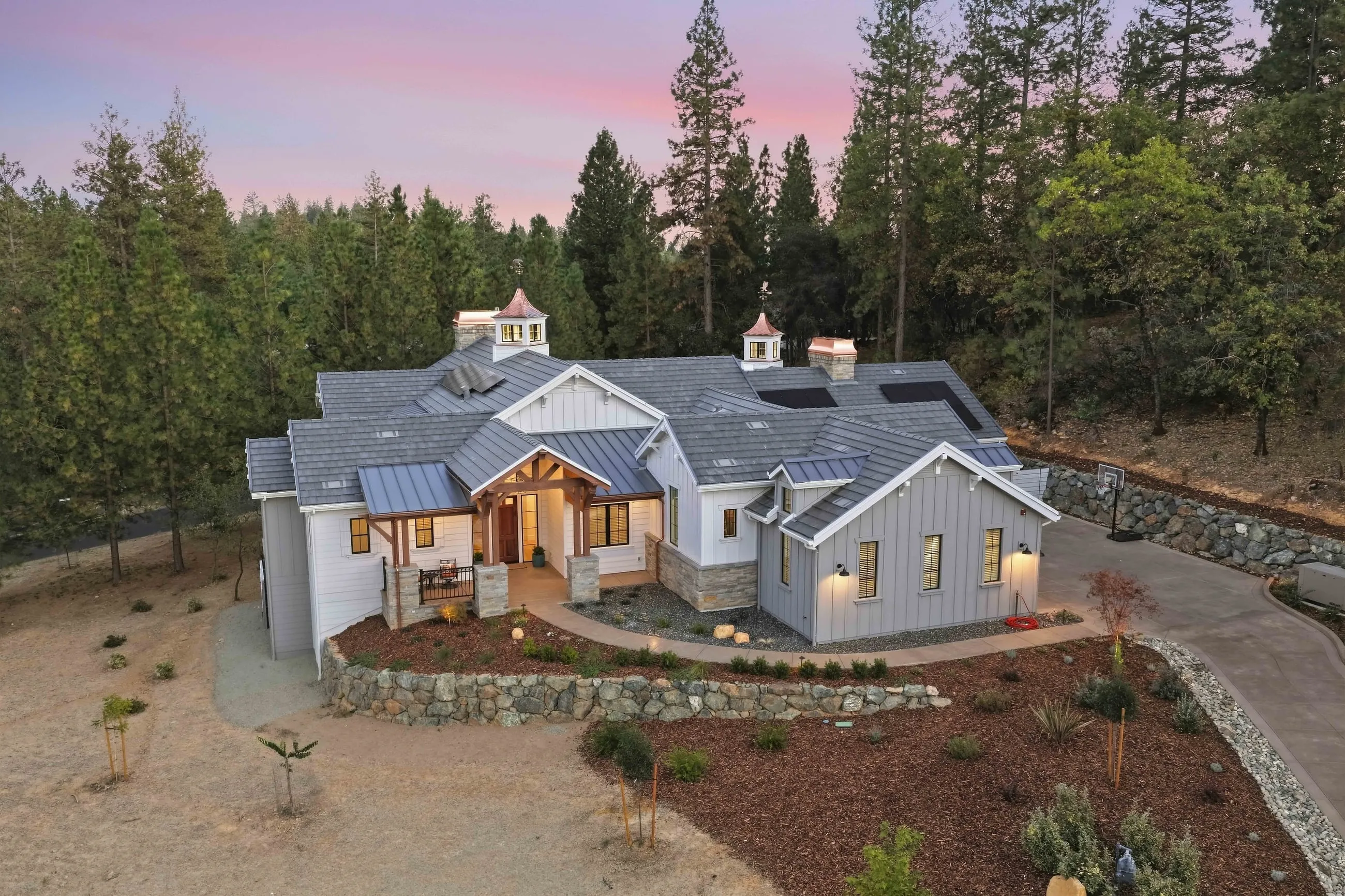 Elevated drone view of the front with gray tile roof, twin cupolas, and a landscaped slope