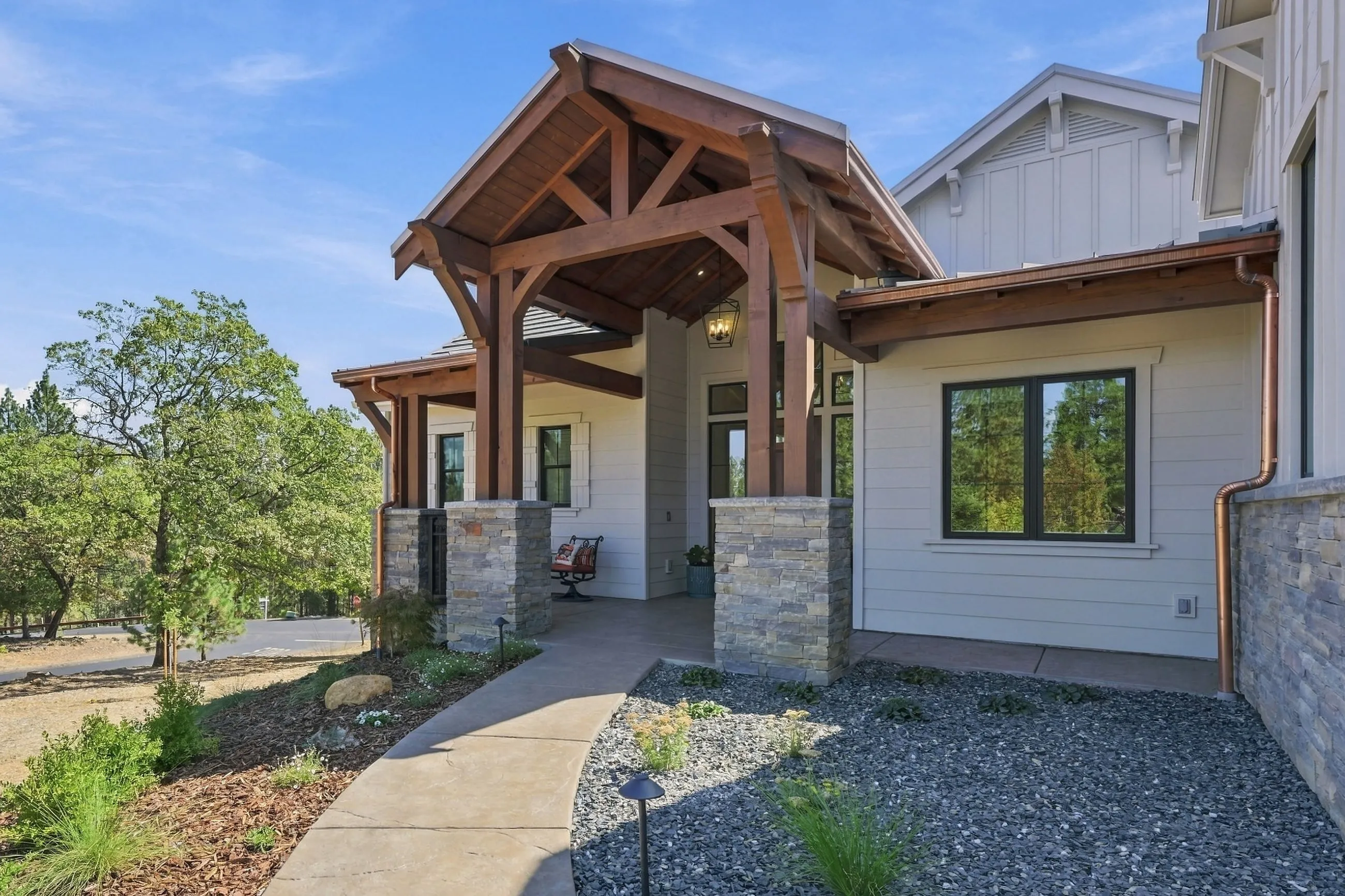 Heavy-timber entry portico on stacked-stone column bases under a blue sky