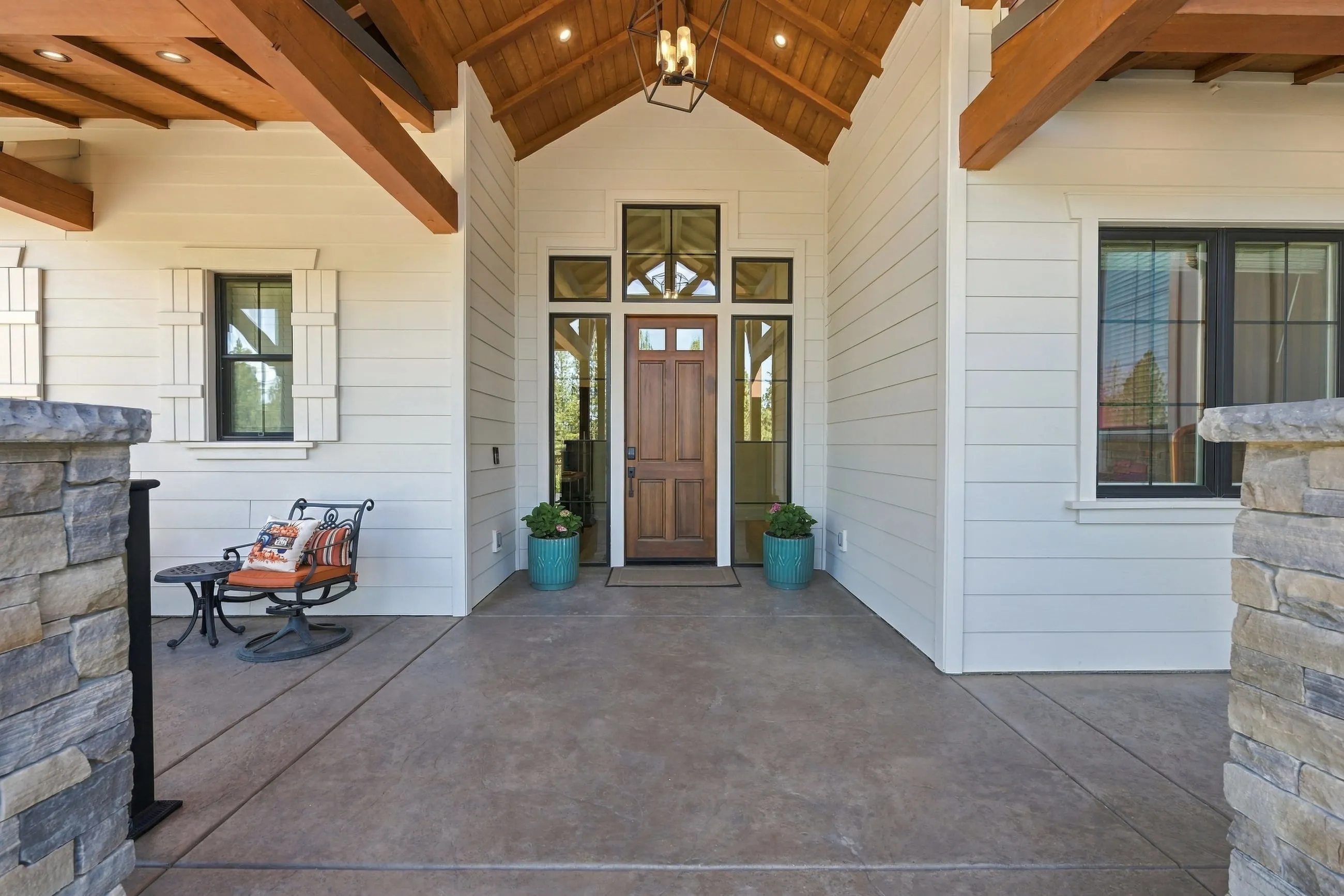 Covered front porch with stained wood ceiling, craftsman front door, and stone piers