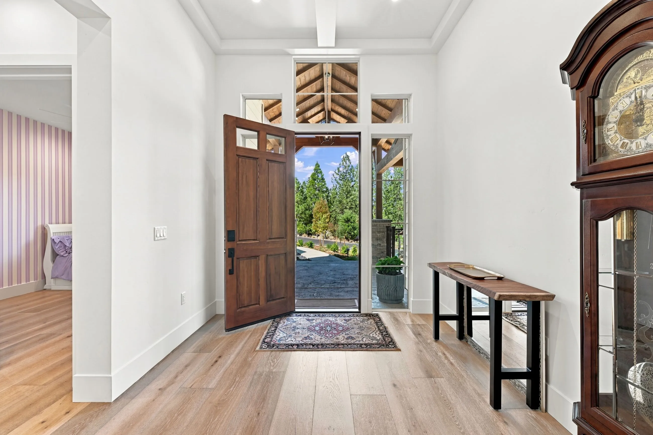 Foyer with the craftsman door open to the pines, wide-plank oak floors, and a grandfather clock