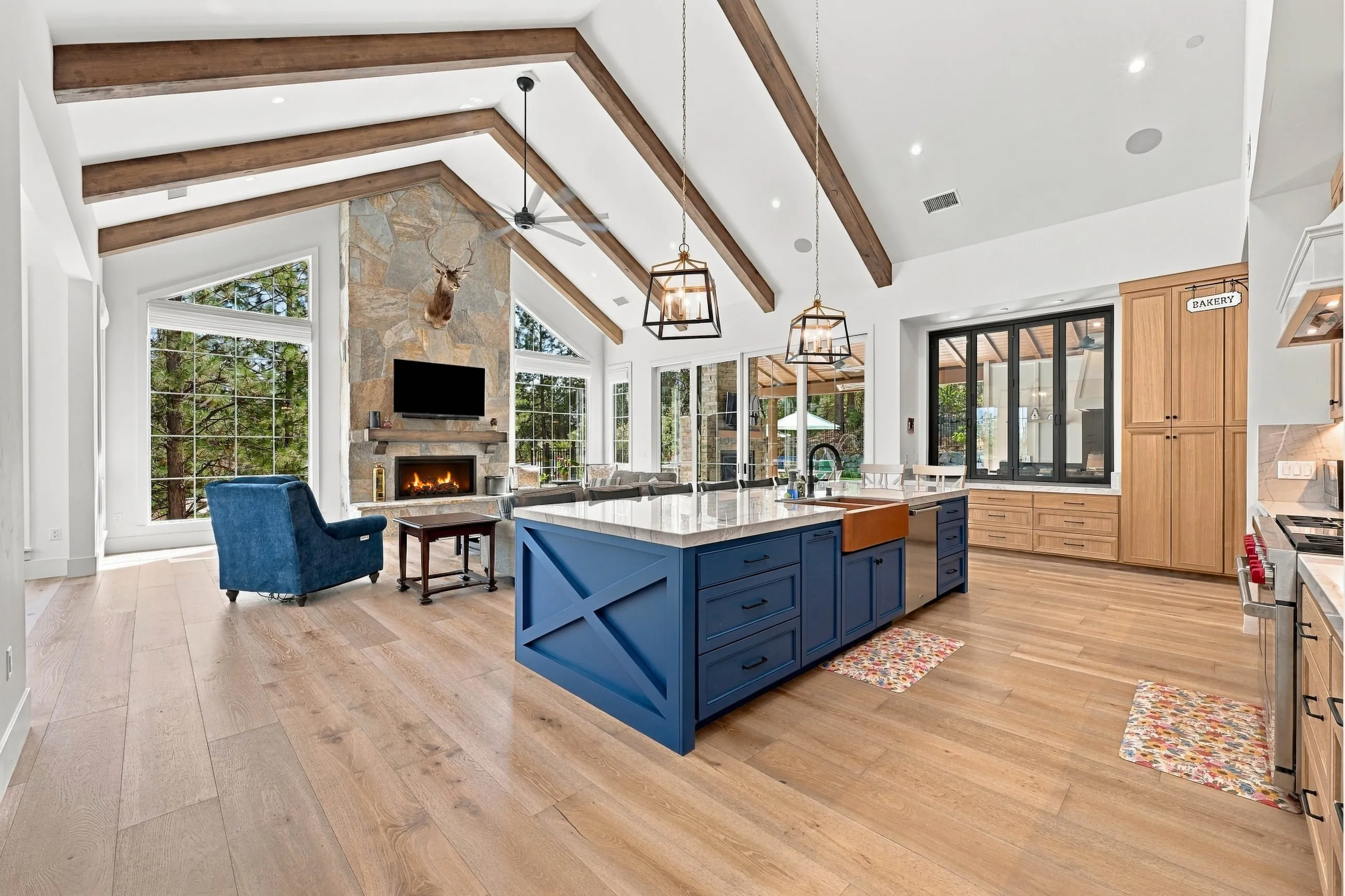 Open great room and kitchen with navy island, exposed stained beams, and stone fireplace