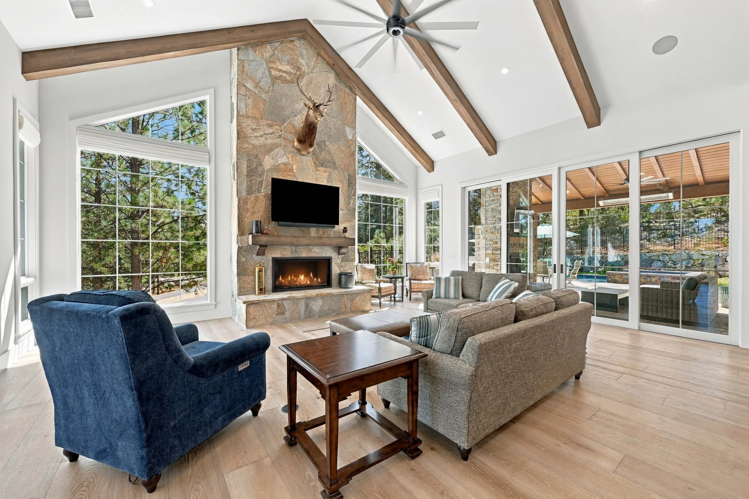 Great room seating beside the stone fireplace with a sliding glass wall opening to the covered patio