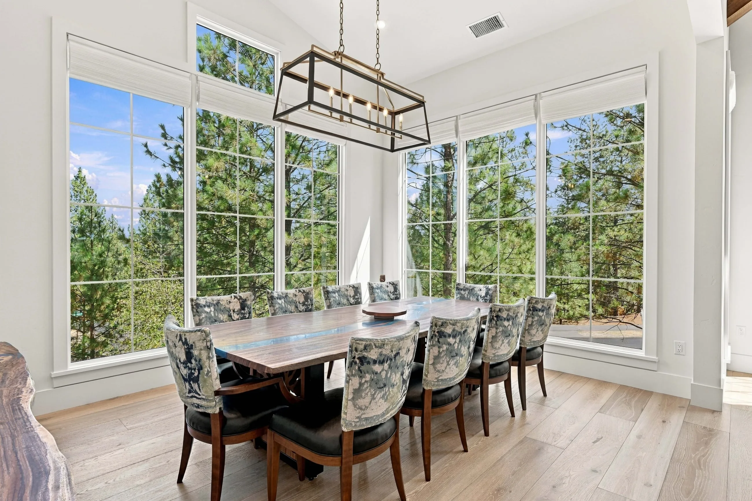 Dining area wrapped in tall windows with forest views under an iron lantern chandelier