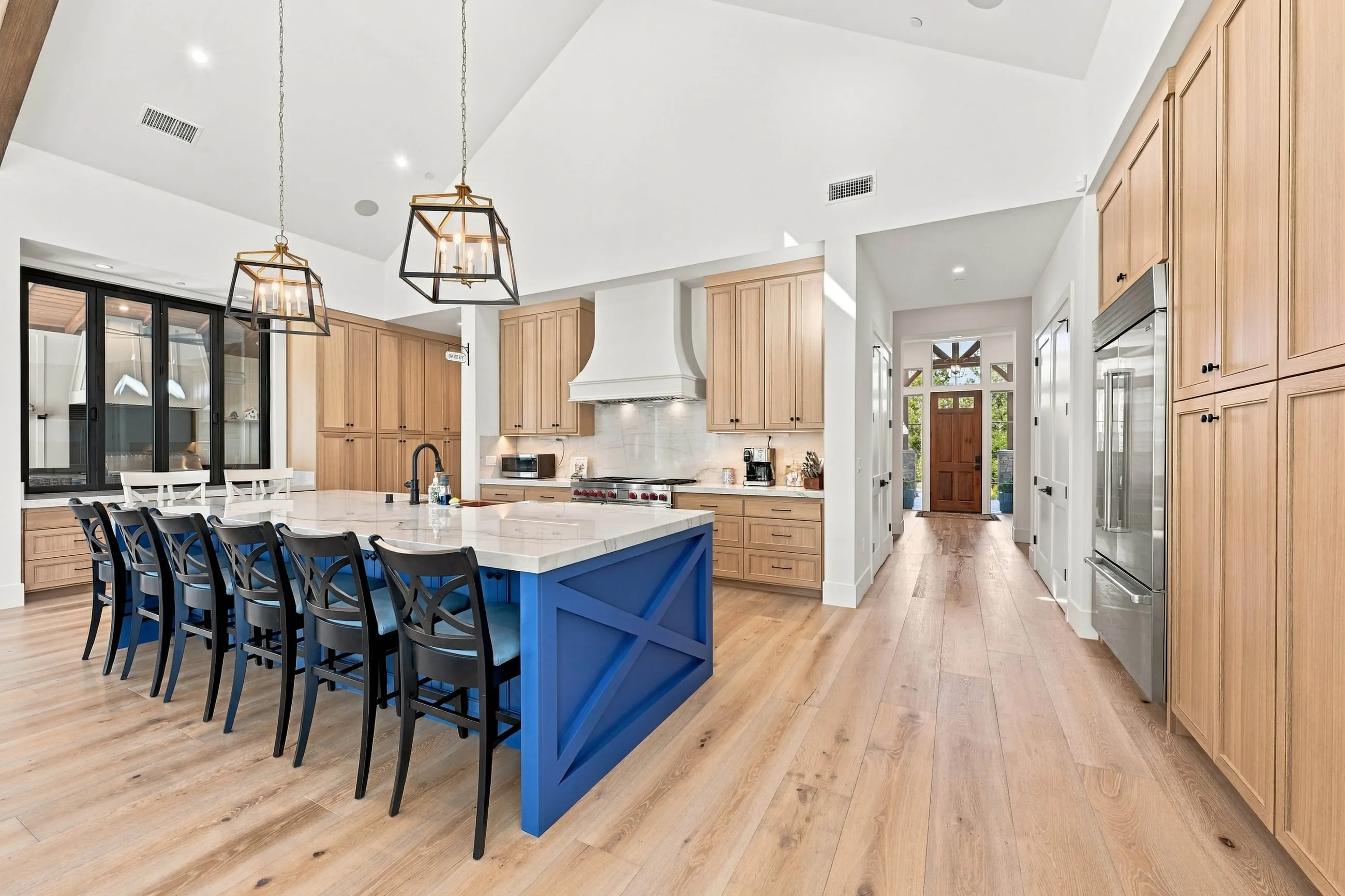 Kitchen with a long navy island seating eight, natural oak cabinetry, and lantern pendants