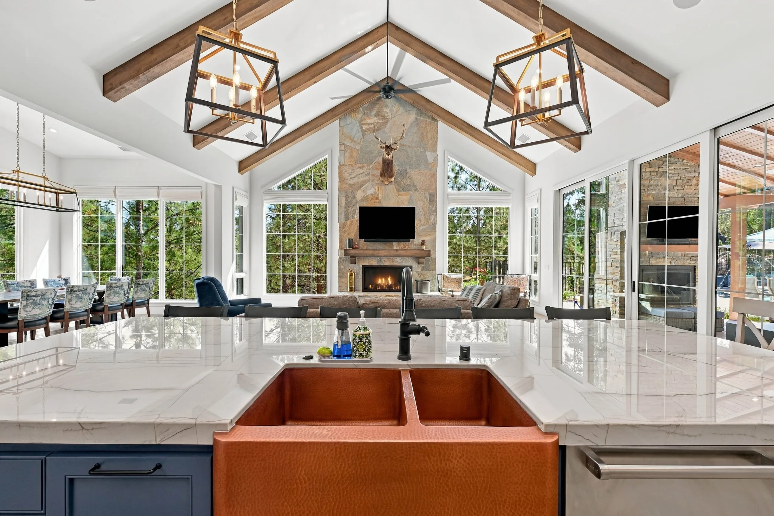 View across a hammered-copper farmhouse sink to the vaulted great room and stone fireplace