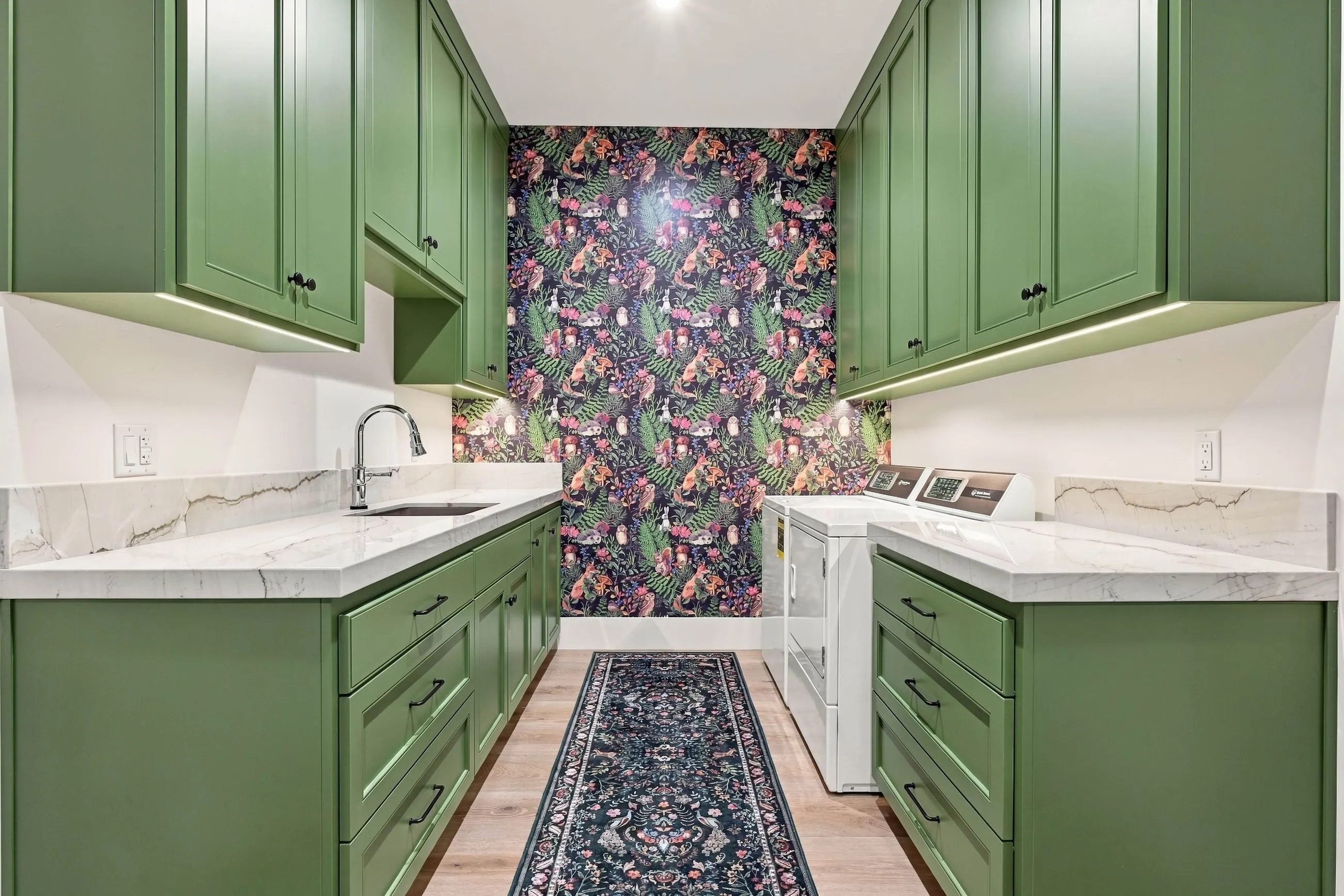 Laundry room with green cabinetry and a bold botanical wallpaper accent wall