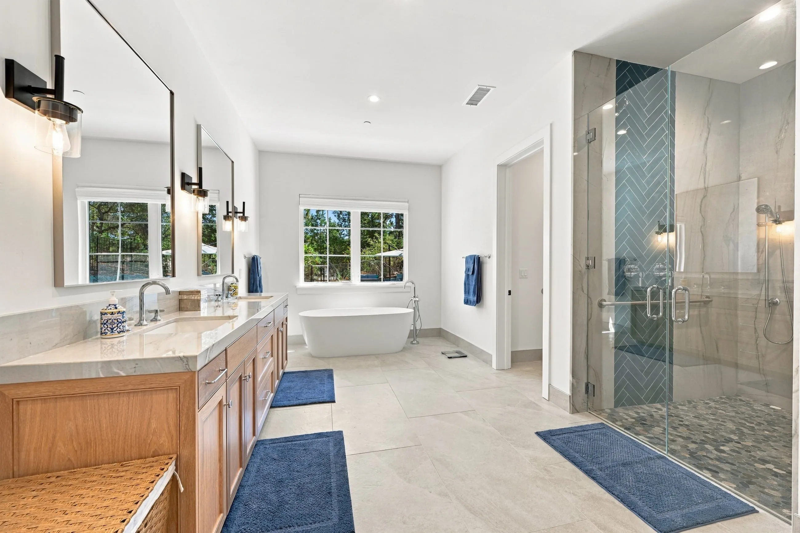 Primary bath with long double vanity, freestanding tub, and glass shower with teal herringbone tile