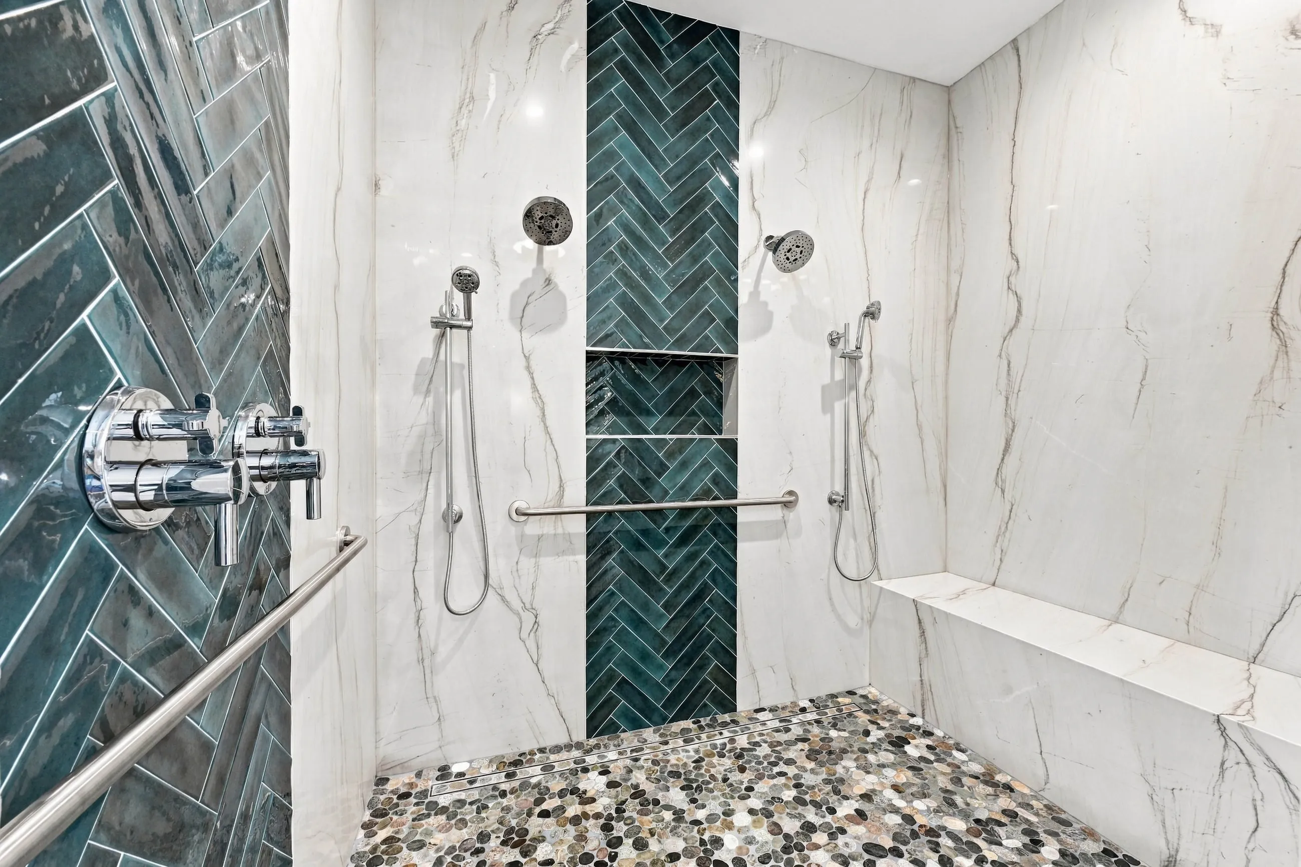 Walk-in shower with marble-look slab walls, teal herringbone accent, and pebble floor