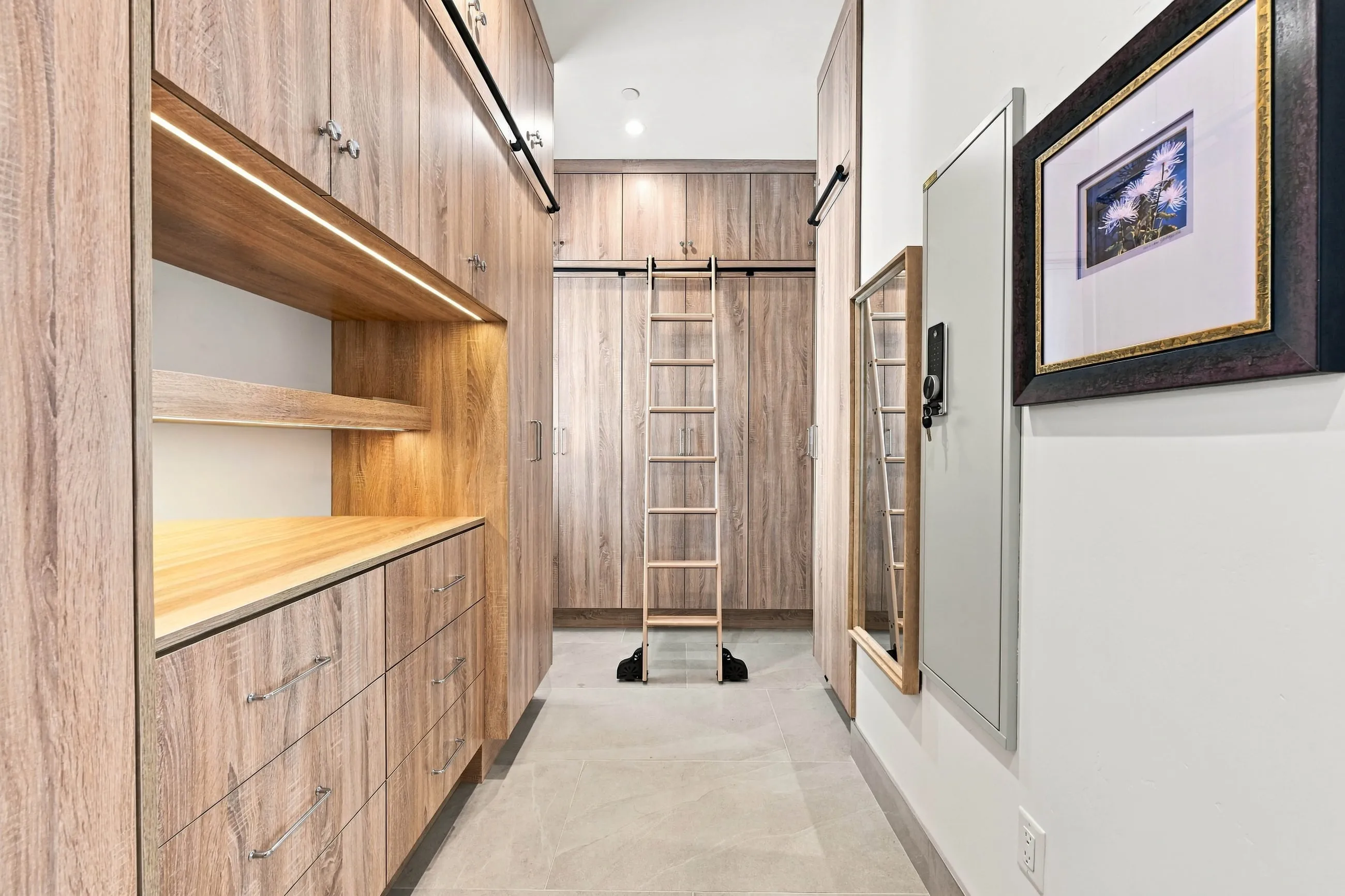Walk-in closet with custom wood cabinetry, lit shelving, and a rolling library ladder