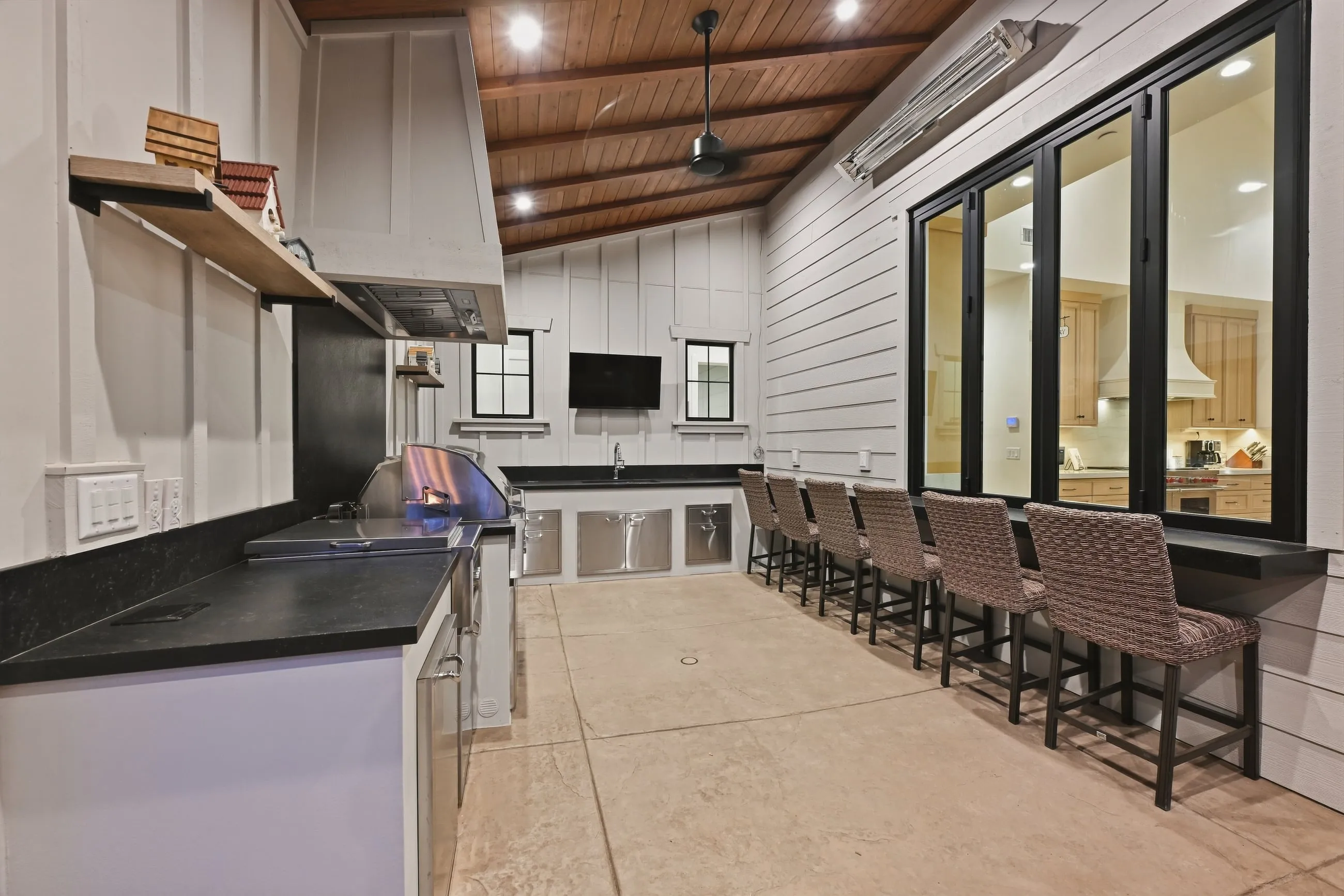 Outdoor kitchen with built-in grill, bar seating, and a pass-through window to the kitchen