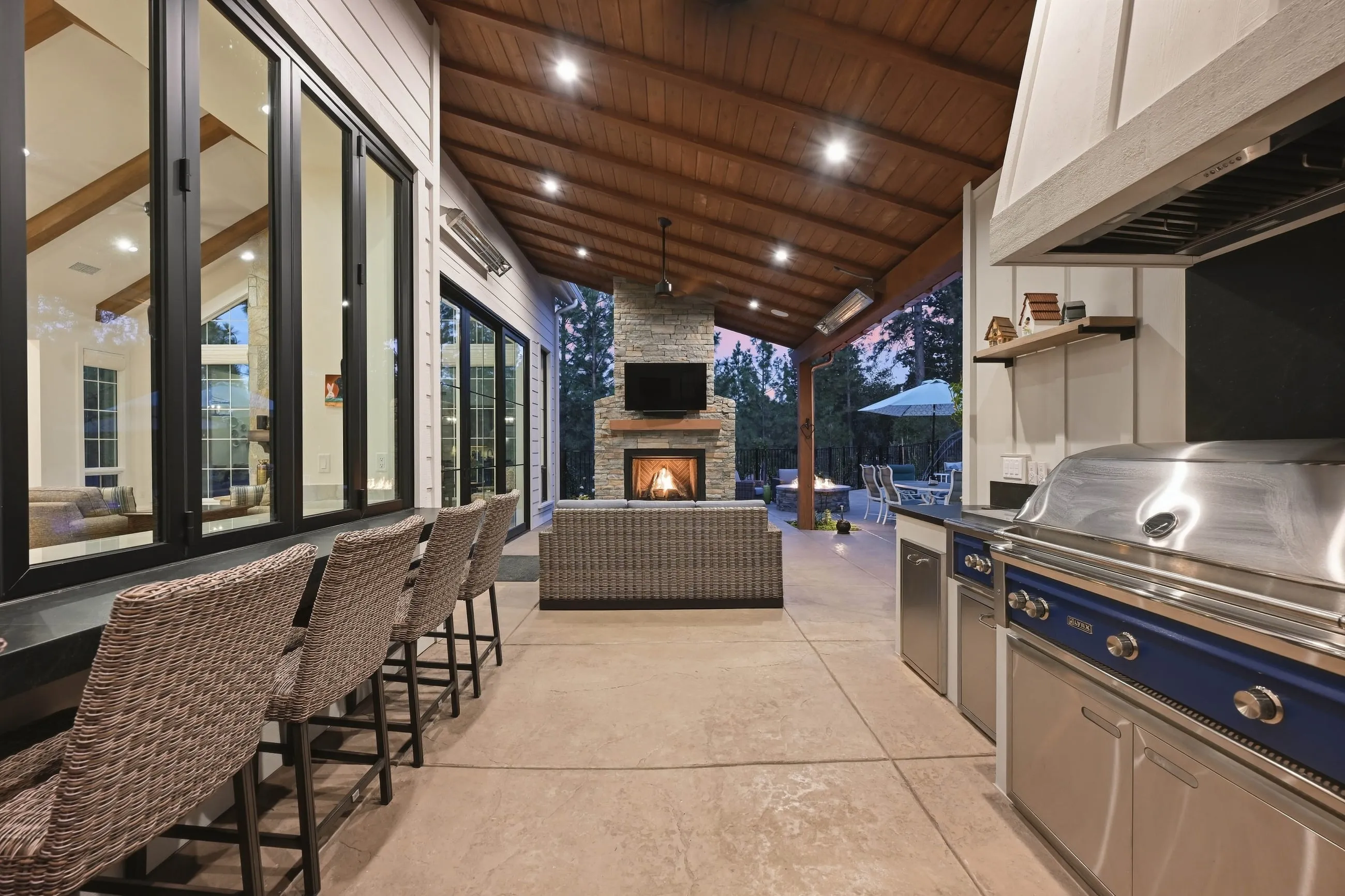 Outdoor kitchen and lounge under a vaulted wood ceiling looking toward the fireplace
