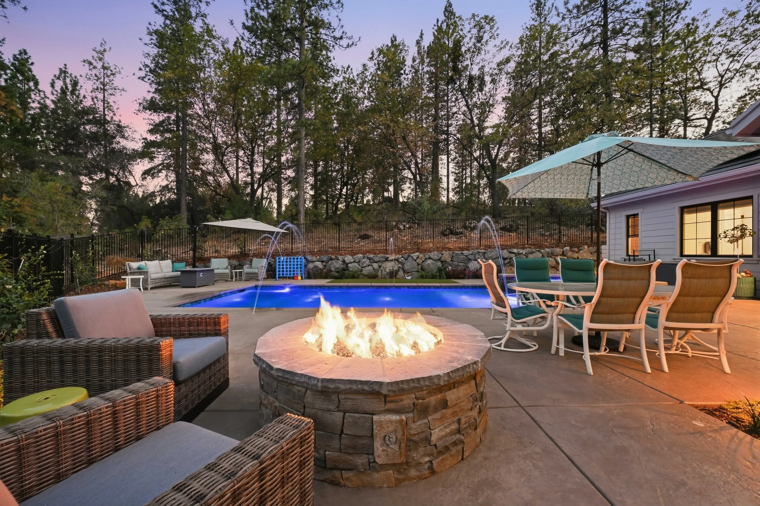 Stone gas fire pit with lounge seating beside the pool at dusk