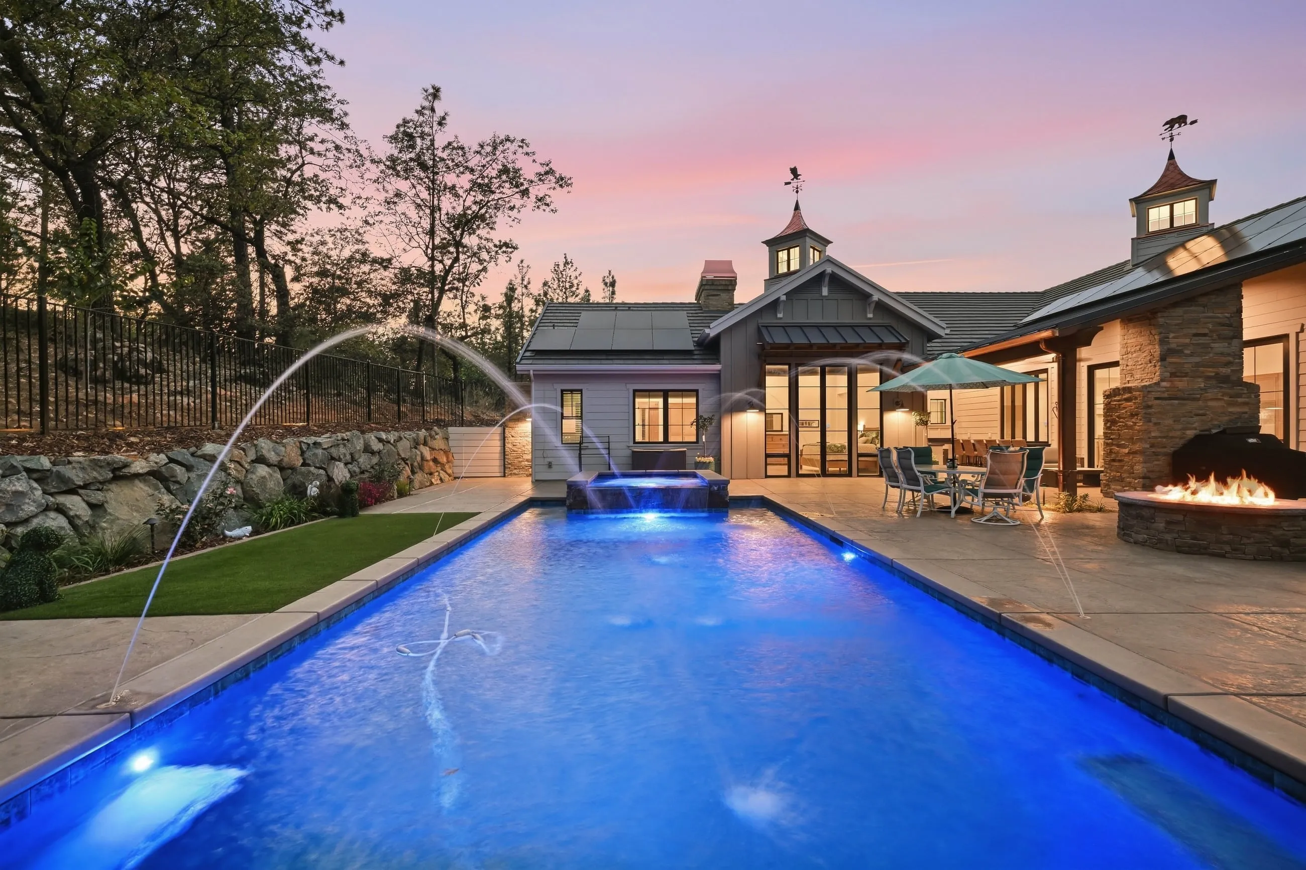 Pool at twilight with arcing water jets and the home glowing beyond