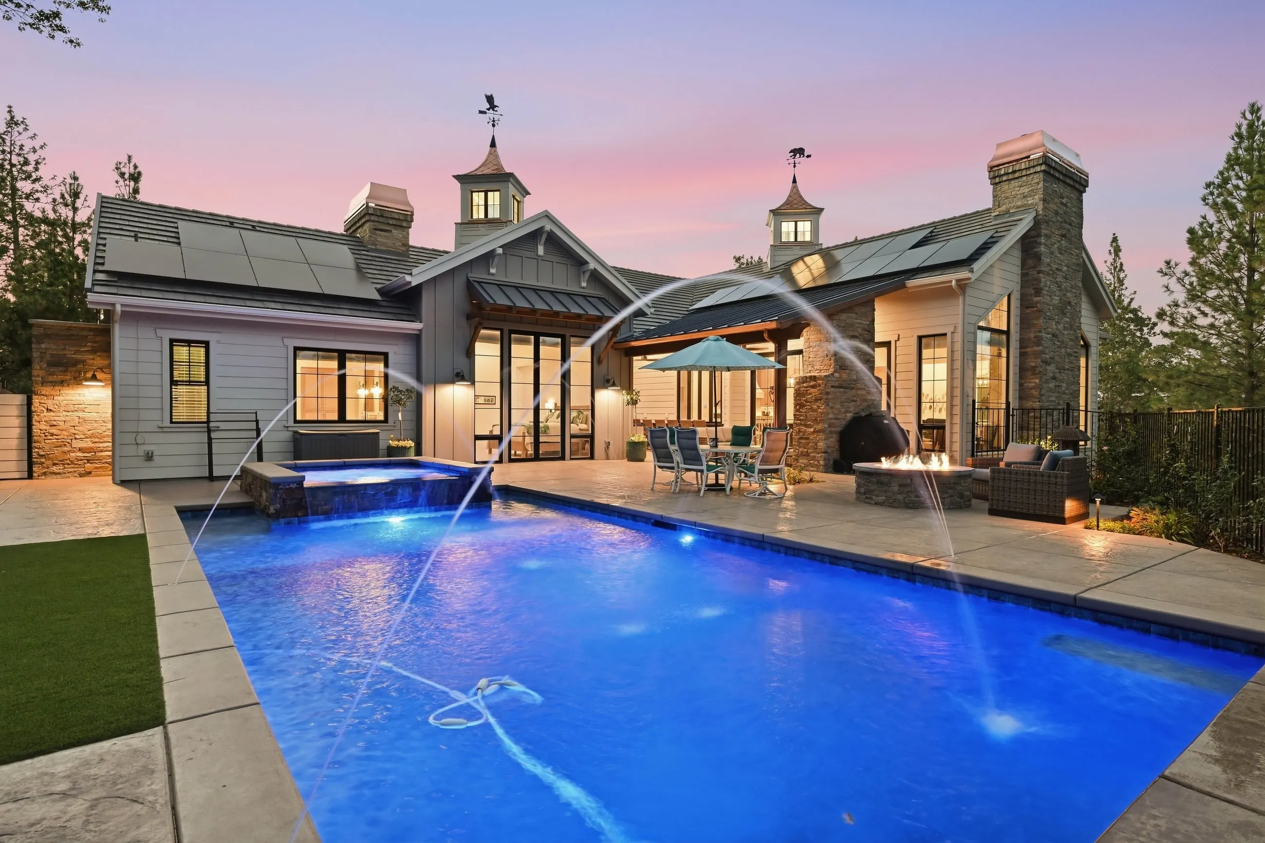 Rear of the farmhouse at dusk with deck jets arcing into the lit pool