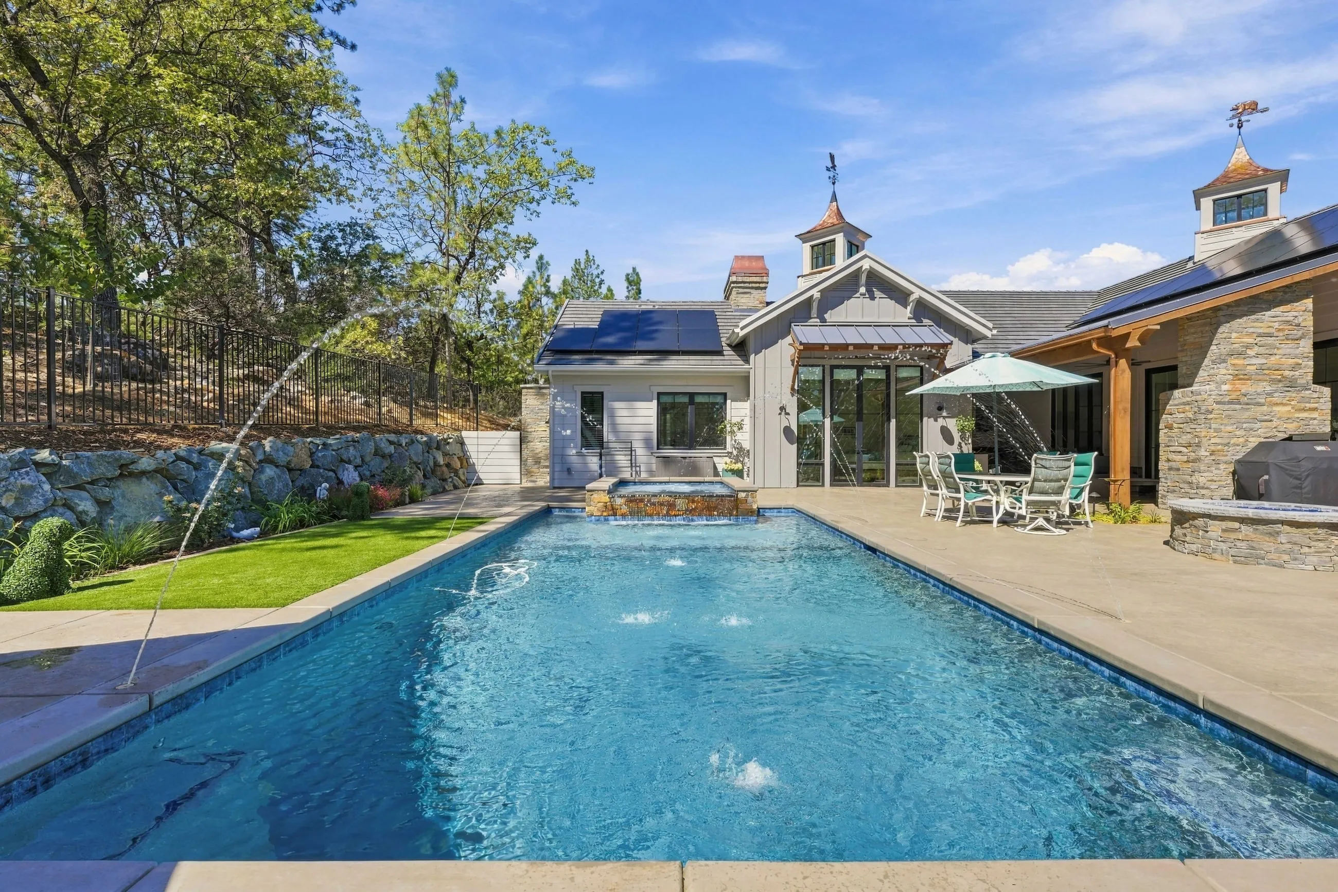 Daytime view of the pool with water arcs and the rear of the farmhouse
