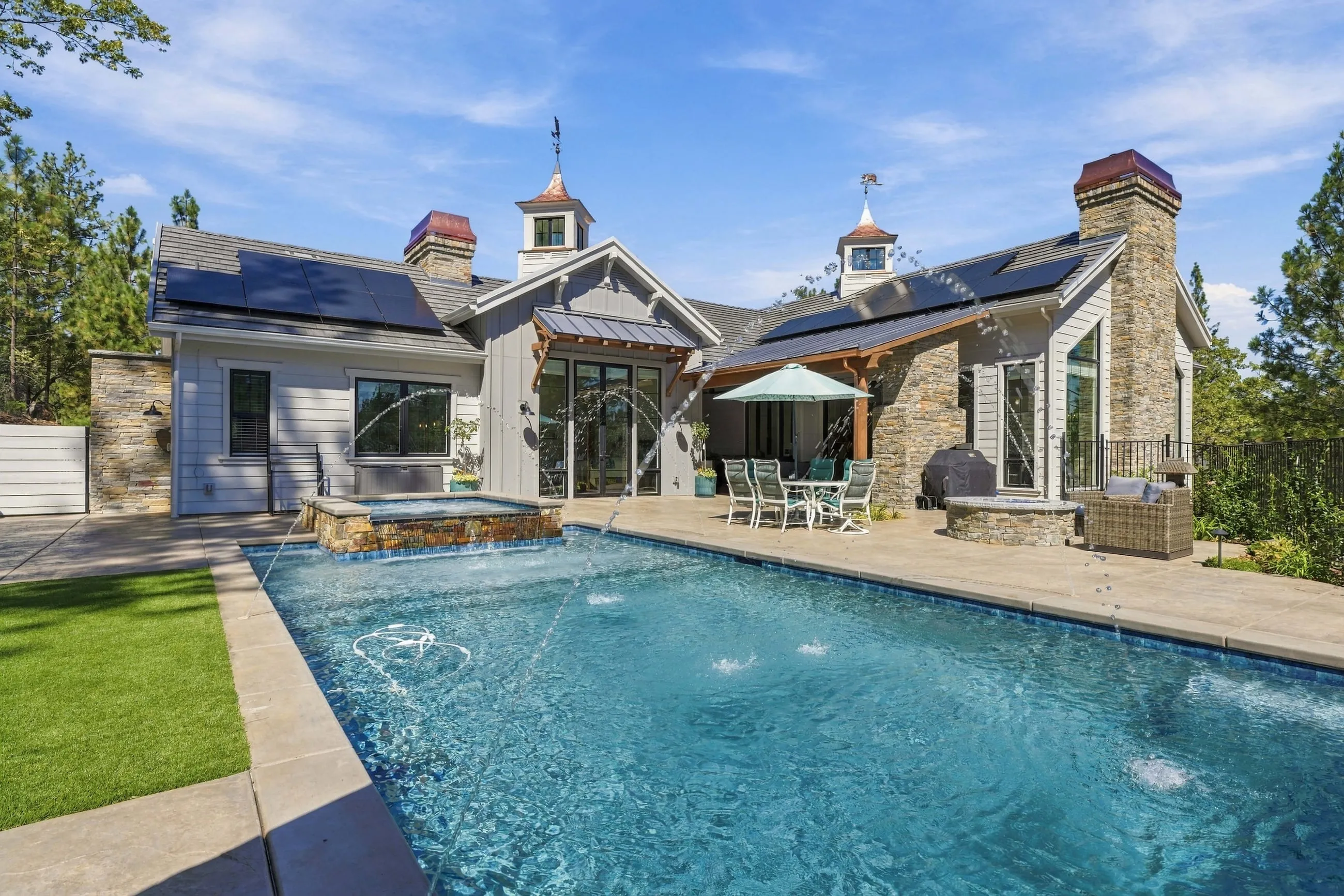 Pool and rear elevation under blue sky with stone chimney and cupolas