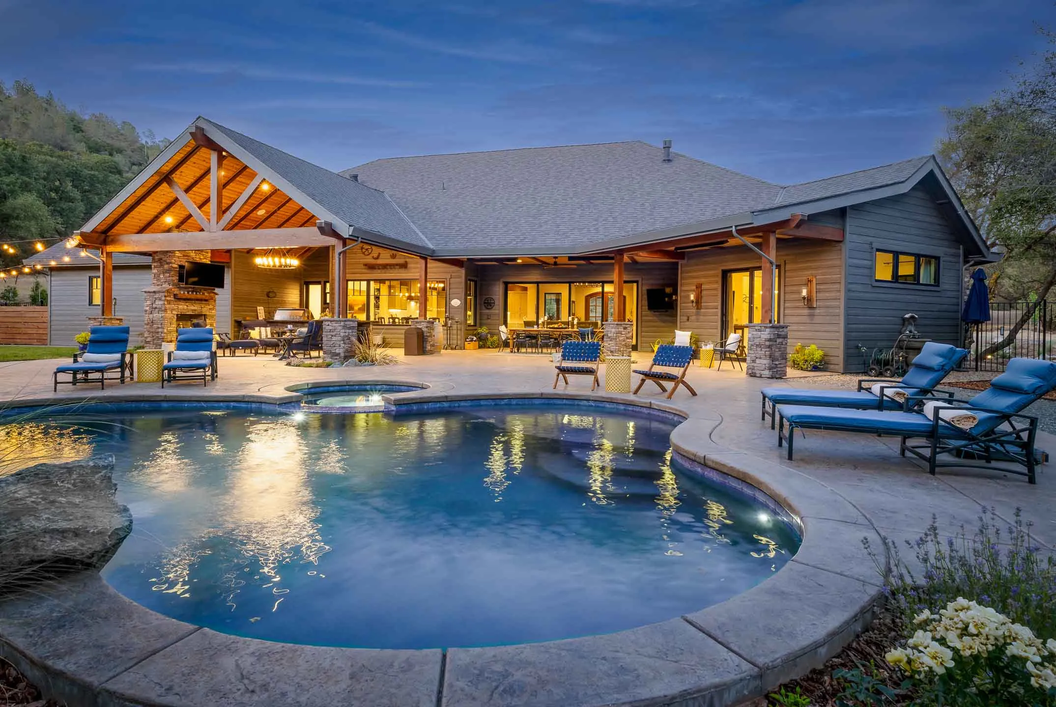 Backyard pool and spa at dusk with a timber-frame pavilion and outdoor kitchen at a Sherman home in Christian Valley