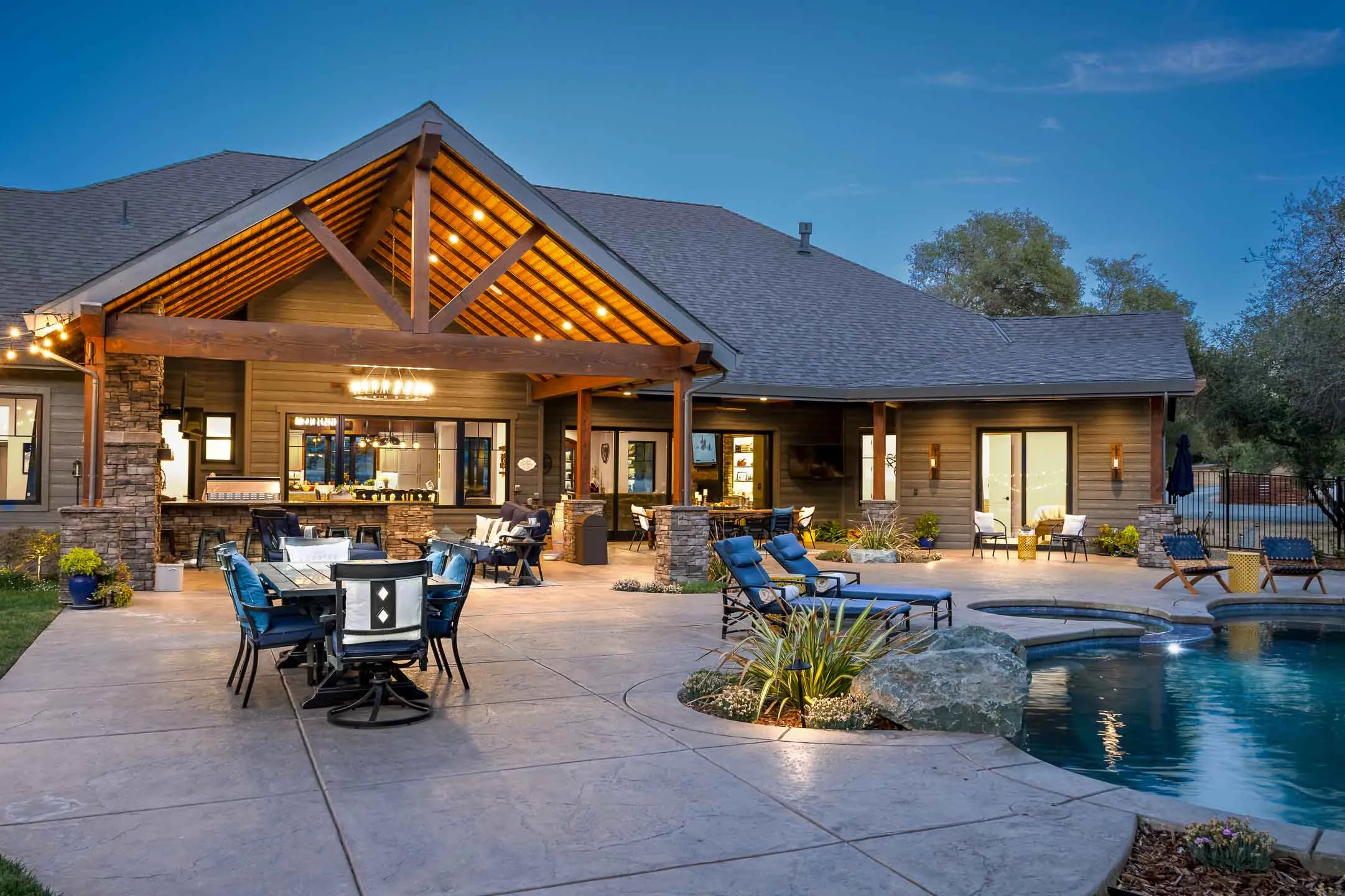 Evening view of a covered outdoor living pavilion with exposed trusses, string lights, and poolside seating at a Sherman home