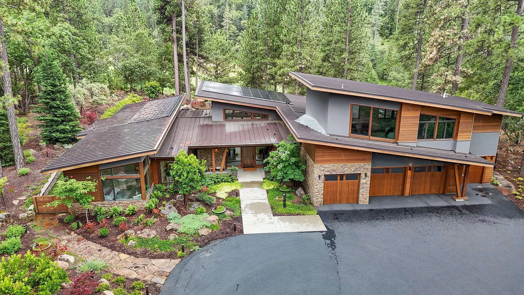 Elevated view of the front with butterfly and shed rooflines, cedar, stucco and stone, set into a wooded lot