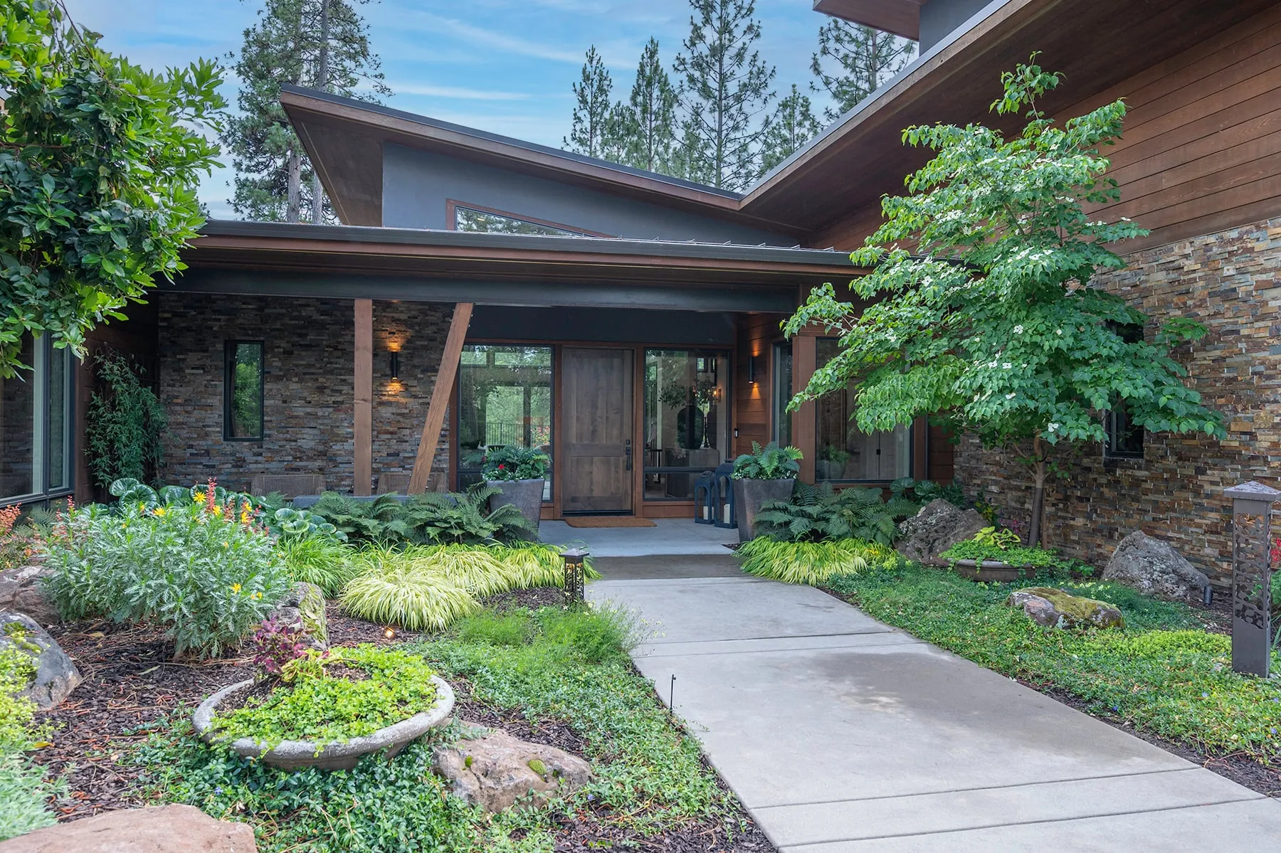 Front porch with timber posts, stacked-stone walls and a solid wood door, reached by a garden path