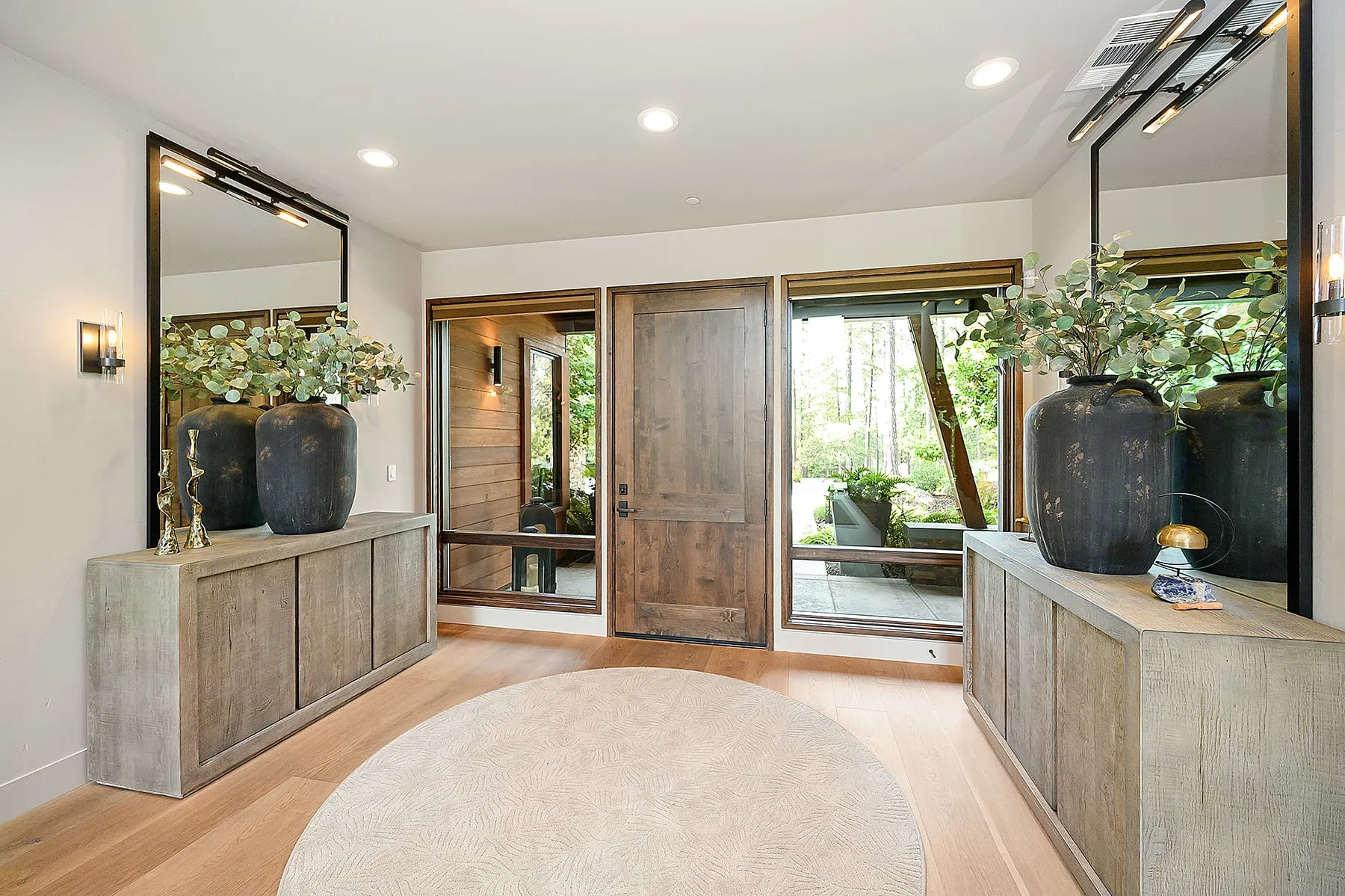 Entry foyer with a wide-plank wood door, glass sidelights, oak floors and matching consoles under large mirrors