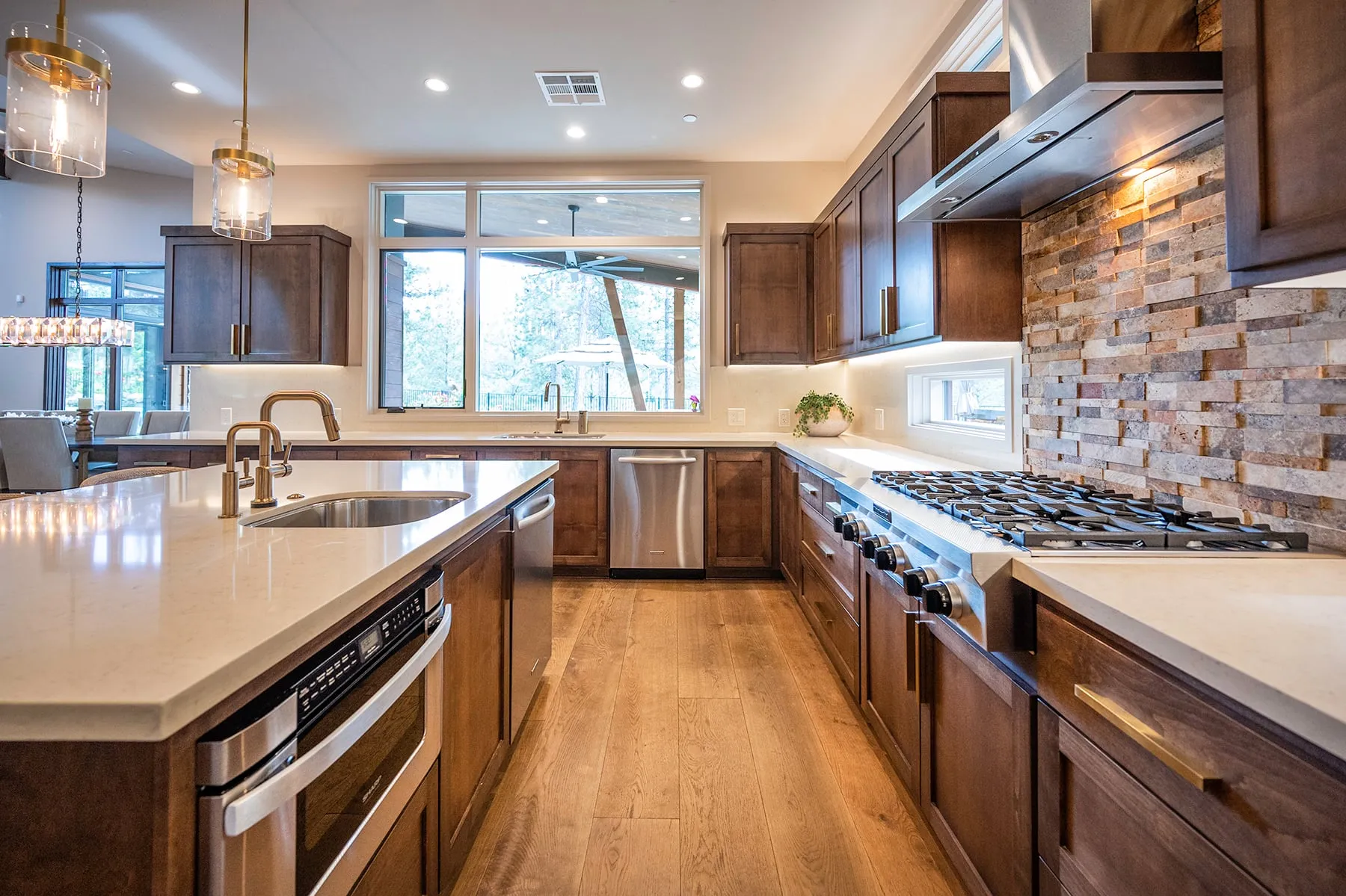 Kitchen with walnut-stained cabinets, a stacked-stone backsplash, a large quartz island and a professional gas range