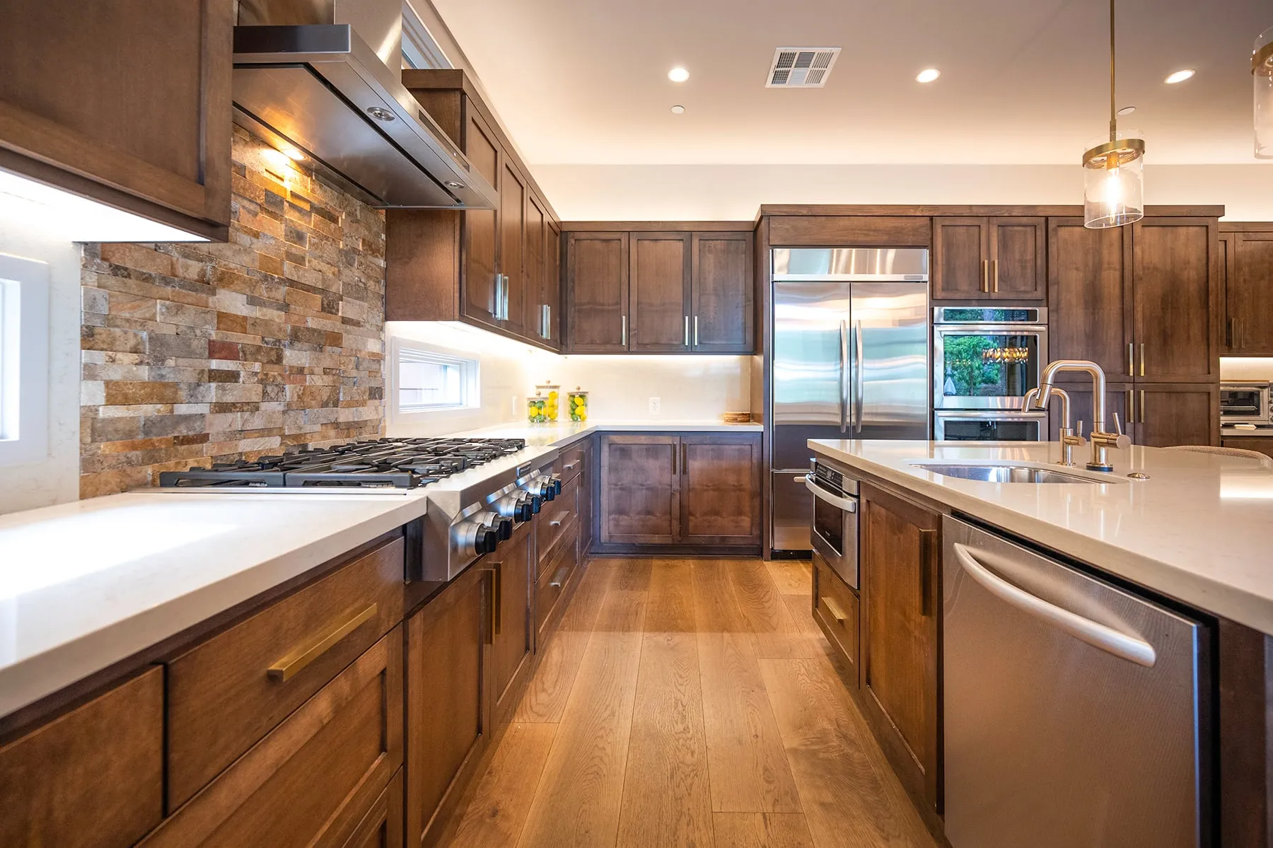 Galley view of the kitchen toward built-in refrigerator and wall ovens, with wood floors and pendant lights