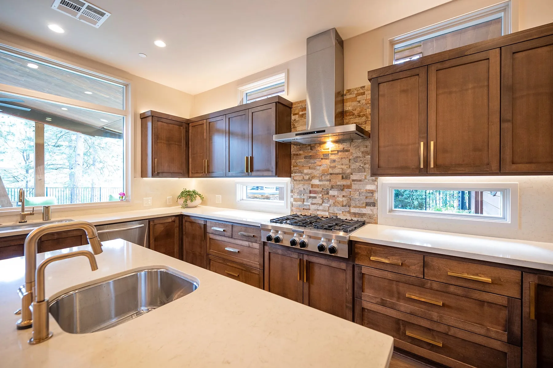Kitchen sink wall with clerestory windows set into the stone backsplash and a stainless hood above the range
