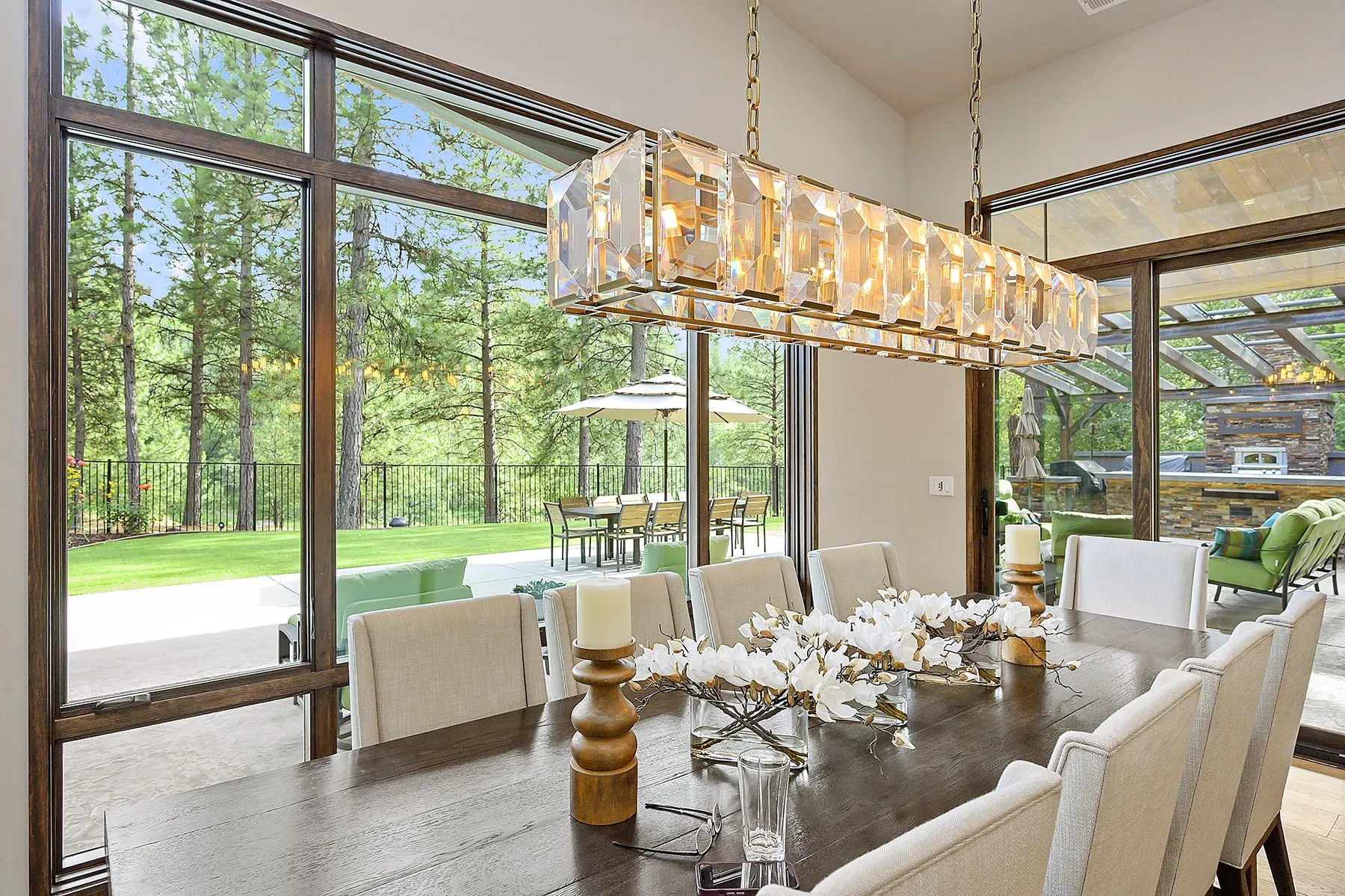 Dining room with a crystal linear chandelier and floor-to-ceiling windows opening to the patio and lawn