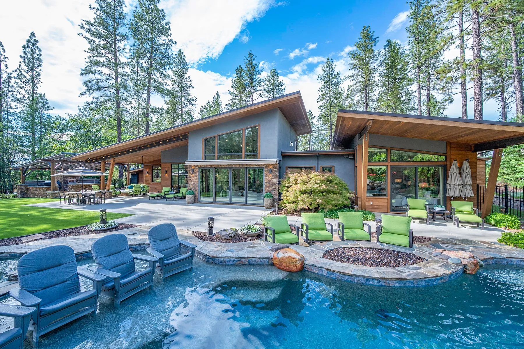 Rear of the home from across the pool, with lounge chairs set into the water, a stone fire pit and walls of glass