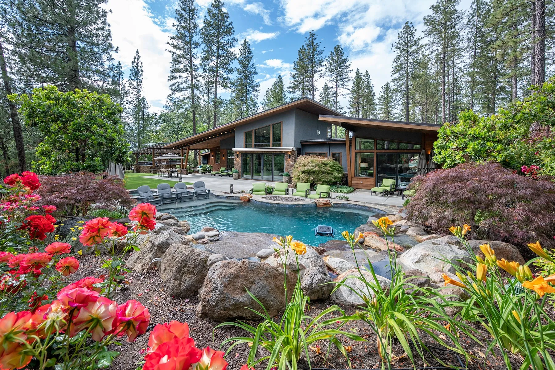 Pool framed by boulders, red geraniums and daylilies, with the home and covered patio beyond