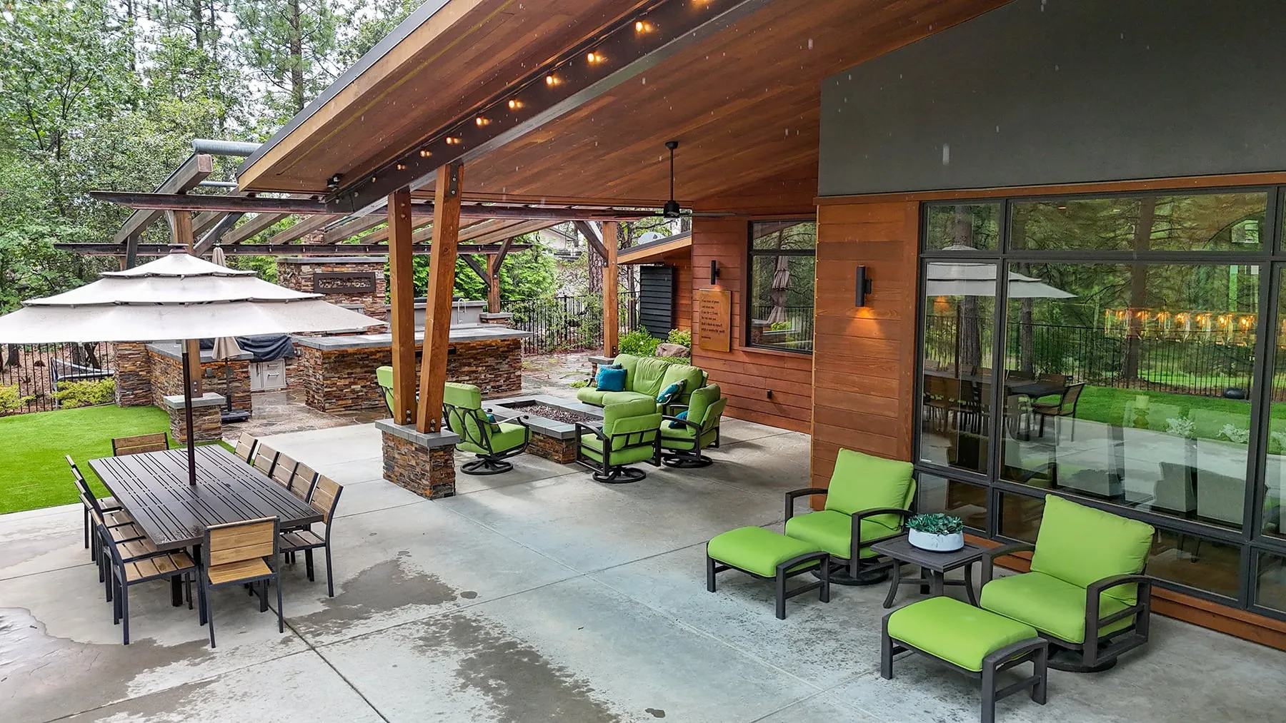 Covered rear patio with a cedar ceiling, outdoor dining and lounge seating beside the glass walls of the great room