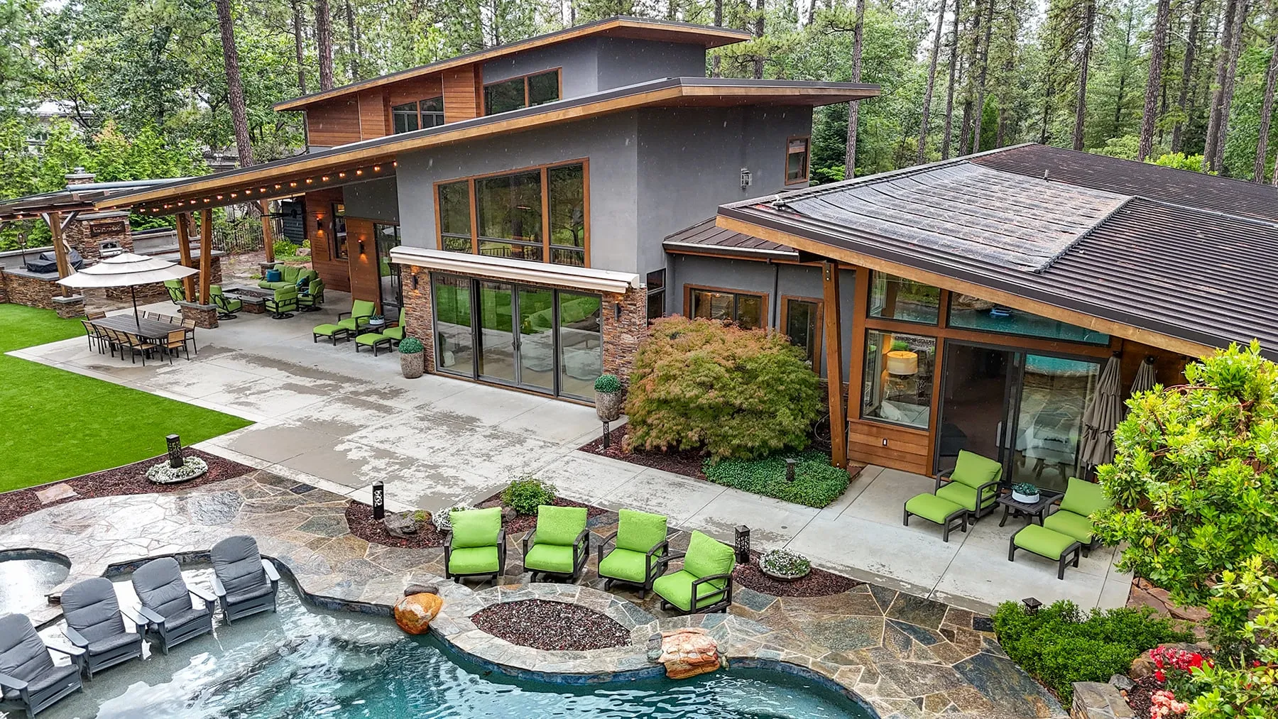 Aerial view of the backyard pool with in-water loungers, fire pit and lounge chairs beside the home