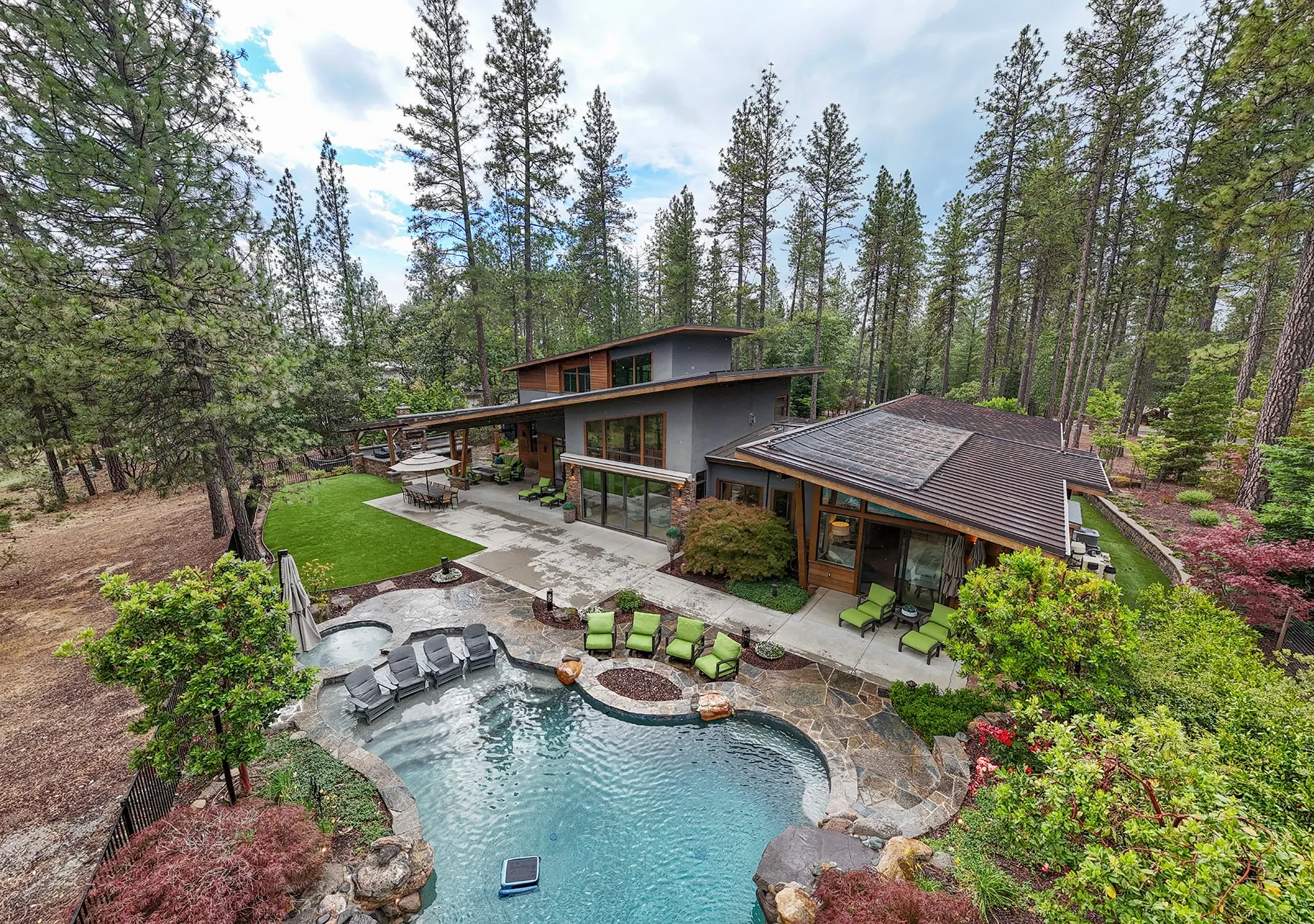 High aerial over the pool and lawn showing the home tucked into the pines