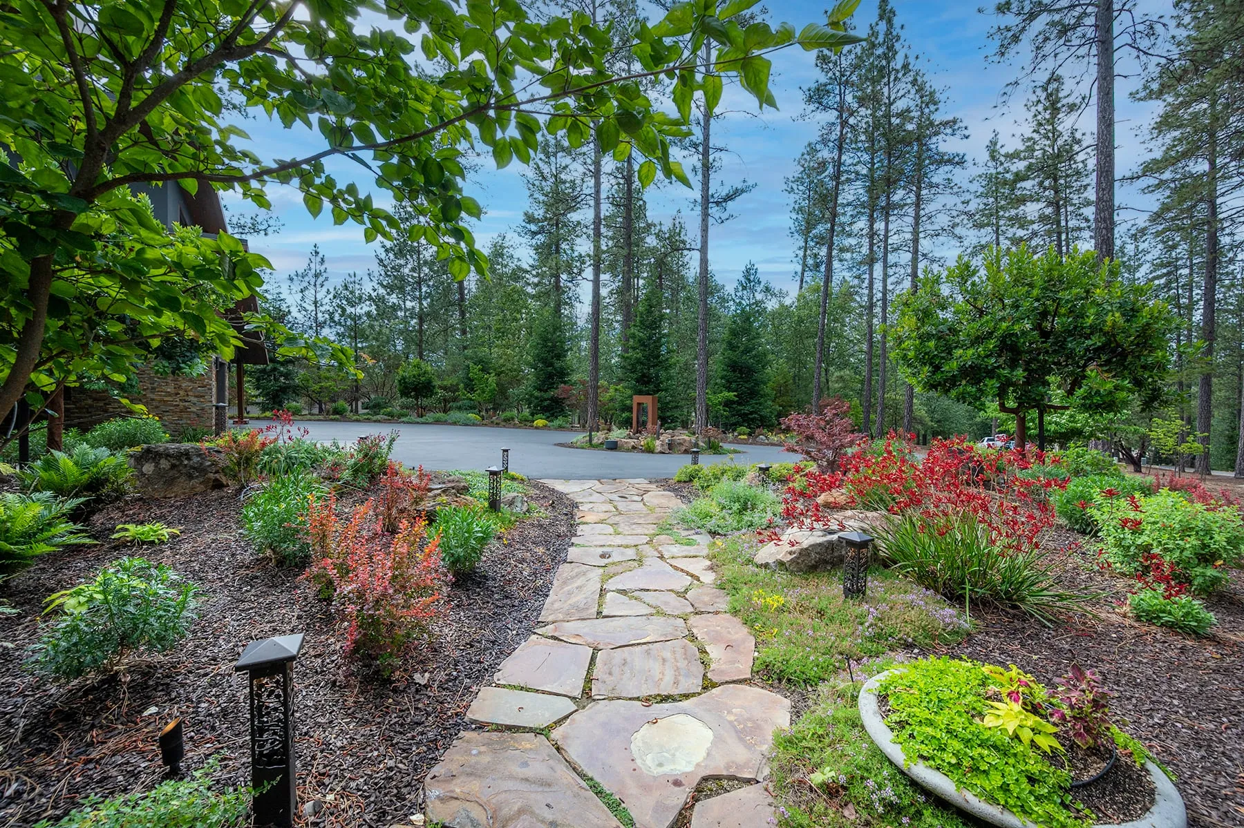 Flagstone garden path winding through red and green plantings toward the driveway