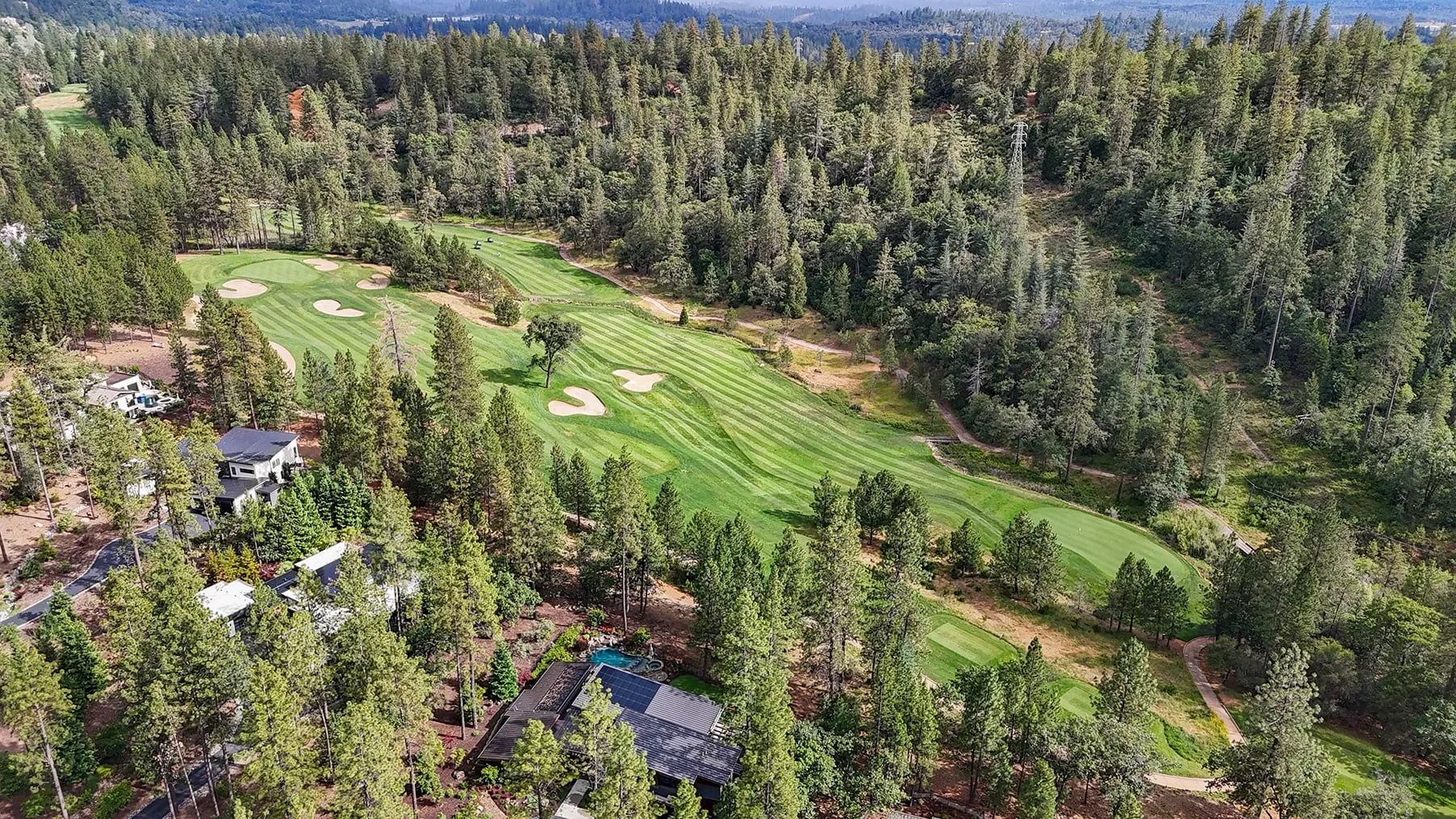Wide aerial of the golf course fairway and greens with the home on its wooded edge